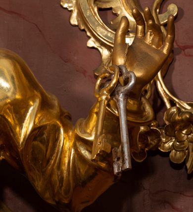 Zdjęcie nr 35: Nastawa ołtarzowa architektoniczna, jednokondygnacyjna ze zwieńczeniem, pięcioosiowa, ustawiona na wysokim cokole. Ołtarz wolnostojący, drewniany, sarkofagowy, wklęsło-wypukły, o zdwojonym froncie; mensa drewniana z marmurowym portatylem. Od frontu rocaille'owy kartusz ujęty fantazyjnymi płycinami oraz liśćmi. Na ołtarzu tabernakulum w formie sześcianu o wklęsłych bokach i wklęsło-wypukłym froncie; ujęte w narożach dwiema parami pilastrów o trzonach przechodzących w spływy wolutowe zdobione rocaille'm i różami. Pilastry podtrzymują falujący gzyms oraz fragmenty falistego, przerwanego, odwróconego przyczółka, przechodzącego w cokół, stanowiący tron wystawienia, na którym stoi krucyfiks. Na ściance frontowej obrotowa nisza, o wykroju stojącego prostokąta zamkniętego łukiem półkolistym, w opasce, zwieńczona kampanulami. W jej polu drzwiczki w formie stojącego prostokąta zamkniętego łukiem półkolistym w profilowanej ramie, z odlewanym przedstawieniem baranka leżącego na księdze z pieczęciami. Tabernakulum ujęte spływami przechodzącymi na krańcach we fragmenty wolutowego gzymsu, na których siedzą figury adorujących aniołów. Ponad tabernakulum fantazyjna ścianka tworząca tło dla tronu wystawienia z prześwitem otoczonym obłokami, z glorią promienistą, flankowana rocaille'owymi uszami. Cokół nastawy z wyodrębnionymi dwoma prostopadłościanami i dwoma konsolami, na dwóch skrajnych osiach bramki zamknięte wolutowymi szczytami tworzącymi cokoły dla figur, z przejściami w formie stojącego prostokąta zamkniętego łukiem odcinkowym nadwieszonym, z drzwiczkami. Cokół i drzwiczki dekorowane rocaille'm. Lico nastawy wklęsłe, osie wydzielone trzema parami pilastrów, na których tle stoją dwie pary kolumn o kapitelach kompozytowych. Podpory dźwigają pełne belkowanie, wyłamane na ich osi, przerwane nad polem środkowym, o gzymsie przechodzącym miejscami w rocaille'owe kartusze. Na osi środkowej wnęka z obrazem Matki Boskiej Wspomożenia Wiernych, w formie stojącego prostokąta zamkniętego łukiem odcinkowym nadwieszonym z uskokiem, ujęta profilowaną ramą, dekorowaną ponad łukiem płomienistym rocaille'm. Na pozostałych czterech osiach figury św. Barbary, św. Apolonii, św. Piotra i św. Pawła ustawione na rokokowych wspornikach. Trzony pilastrów i pola osi bocznych wypełnione rocaille'm, fryz dekorowany zwisami kwiatowymi. Zwieńczenie w formie zbliżonej do trapezu, zamknięte dwoma fragmentami gzymsu przechodzącego w woluty, flankowane wolutami spływającymi na belkowanie wewnętrznej pary kolumn, na których siedzą adorujące figury aniołów. W polu rzeźbiarska grupa Trójcy Świętej, pośród obłoków, w glorii promienistej, zwieńczona gołębicą Ducha Świętego w otoku z obłoków i uskrzydlonych główek anielskich, w glorii promienistej, flankowana przez dwa putta siedzące na gzymsie. Zwieńczenie po bokach obwiedzione rocaille'm, ujęte liśćmi palmowymi. Na belkowaniu, na osiach zewnętrznej pary kolumn wolutowe cokoły z rokokowymi wazonami. Struktura polichromowana na sposób imitujący marmoryzację w kolorze różowym i różowo-pomarańczowym, kolumny, profile i ornamentyka złocone, obłoki srebrzone. 

