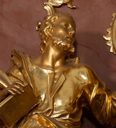 Zdjęcie nr 38: Nastawa ołtarzowa architektoniczna, jednokondygnacyjna ze zwieńczeniem, pięcioosiowa, ustawiona na wysokim cokole. Ołtarz wolnostojący, drewniany, sarkofagowy, wklęsło-wypukły, o zdwojonym froncie; mensa drewniana z marmurowym portatylem. Od frontu rocaille&#039;owy kartusz ujęty fantazyjnymi płycinami oraz liśćmi. Na ołtarzu tabernakulum w formie sześcianu o wklęsłych bokach i wklęsło-wypukłym froncie; ujęte w narożach dwiema parami pilastrów o trzonach przechodzących w spływy wolutowe zdobione rocaille&#039;m i różami. Pilastry podtrzymują falujący gzyms oraz fragmenty falistego, przerwanego, odwróconego przyczółka, przechodzącego w cokół, stanowiący tron wystawienia, na którym stoi krucyfiks. Na ściance frontowej obrotowa nisza, o wykroju stojącego prostokąta zamkniętego łukiem półkolistym, w opasce, zwieńczona kampanulami. W jej polu drzwiczki w formie stojącego prostokąta zamkniętego łukiem półkolistym w profilowanej ramie, z odlewanym przedstawieniem baranka leżącego na księdze z pieczęciami. Tabernakulum ujęte spływami przechodzącymi na krańcach we fragmenty wolutowego gzymsu, na których siedzą figury adorujących aniołów. Ponad tabernakulum fantazyjna ścianka tworząca tło dla tronu wystawienia z prześwitem otoczonym obłokami, z glorią promienistą, flankowana rocaille&#039;owymi uszami. Cokół nastawy z wyodrębnionymi dwoma prostopadłościanami i dwoma konsolami, na dwóch skrajnych osiach bramki zamknięte wolutowymi szczytami tworzącymi cokoły dla figur, z przejściami w formie stojącego prostokąta zamkniętego łukiem odcinkowym nadwieszonym, z drzwiczkami. Cokół i drzwiczki dekorowane rocaille&#039;m. Lico nastawy wklęsłe, osie wydzielone trzema parami pilastrów, na których tle stoją dwie pary kolumn o kapitelach kompozytowych. Podpory dźwigają pełne belkowanie, wyłamane na ich osi, przerwane nad polem środkowym, o gzymsie przechodzącym miejscami w rocaille&#039;owe kartusze. Na osi środkowej wnęka z obrazem Matki Boskiej Wspomożenia Wiernych, w formie stojącego prostokąta zamkniętego łukiem odcinkowym nadwieszonym z uskokiem, ujęta profilowaną ramą, dekorowaną ponad łukiem płomienistym rocaille&#039;m. Na pozostałych czterech osiach figury św. Barbary, św. Apolonii, św. Piotra i św. Pawła ustawione na rokokowych wspornikach. Trzony pilastrów i pola osi bocznych wypełnione rocaille&#039;m, fryz dekorowany zwisami kwiatowymi. Zwieńczenie w formie zbliżonej do trapezu, zamknięte dwoma fragmentami gzymsu przechodzącego w woluty, flankowane wolutami spływającymi na belkowanie wewnętrznej pary kolumn, na których siedzą adorujące figury aniołów. W polu rzeźbiarska grupa Trójcy Świętej, pośród obłoków, w glorii promienistej, zwieńczona gołębicą Ducha Świętego w otoku z obłoków i uskrzydlonych główek anielskich, w glorii promienistej, flankowana przez dwa putta siedzące na gzymsie. Zwieńczenie po bokach obwiedzione rocaille&#039;m, ujęte liśćmi palmowymi. Na belkowaniu, na osiach zewnętrznej pary kolumn wolutowe cokoły z rokokowymi wazonami. Struktura polichromowana na sposób imitujący marmoryzację w kolorze różowym i różowo-pomarańczowym, kolumny, profile i ornamentyka złocone, obłoki srebrzone. 

