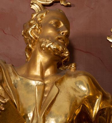 Zdjęcie nr 37: Nastawa ołtarzowa architektoniczna, jednokondygnacyjna ze zwieńczeniem, pięcioosiowa, ustawiona na wysokim cokole. Ołtarz wolnostojący, drewniany, sarkofagowy, wklęsło-wypukły, o zdwojonym froncie; mensa drewniana z marmurowym portatylem. Od frontu rocaille'owy kartusz ujęty fantazyjnymi płycinami oraz liśćmi. Na ołtarzu tabernakulum w formie sześcianu o wklęsłych bokach i wklęsło-wypukłym froncie; ujęte w narożach dwiema parami pilastrów o trzonach przechodzących w spływy wolutowe zdobione rocaille'm i różami. Pilastry podtrzymują falujący gzyms oraz fragmenty falistego, przerwanego, odwróconego przyczółka, przechodzącego w cokół, stanowiący tron wystawienia, na którym stoi krucyfiks. Na ściance frontowej obrotowa nisza, o wykroju stojącego prostokąta zamkniętego łukiem półkolistym, w opasce, zwieńczona kampanulami. W jej polu drzwiczki w formie stojącego prostokąta zamkniętego łukiem półkolistym w profilowanej ramie, z odlewanym przedstawieniem baranka leżącego na księdze z pieczęciami. Tabernakulum ujęte spływami przechodzącymi na krańcach we fragmenty wolutowego gzymsu, na których siedzą figury adorujących aniołów. Ponad tabernakulum fantazyjna ścianka tworząca tło dla tronu wystawienia z prześwitem otoczonym obłokami, z glorią promienistą, flankowana rocaille'owymi uszami. Cokół nastawy z wyodrębnionymi dwoma prostopadłościanami i dwoma konsolami, na dwóch skrajnych osiach bramki zamknięte wolutowymi szczytami tworzącymi cokoły dla figur, z przejściami w formie stojącego prostokąta zamkniętego łukiem odcinkowym nadwieszonym, z drzwiczkami. Cokół i drzwiczki dekorowane rocaille'm. Lico nastawy wklęsłe, osie wydzielone trzema parami pilastrów, na których tle stoją dwie pary kolumn o kapitelach kompozytowych. Podpory dźwigają pełne belkowanie, wyłamane na ich osi, przerwane nad polem środkowym, o gzymsie przechodzącym miejscami w rocaille'owe kartusze. Na osi środkowej wnęka z obrazem Matki Boskiej Wspomożenia Wiernych, w formie stojącego prostokąta zamkniętego łukiem odcinkowym nadwieszonym z uskokiem, ujęta profilowaną ramą, dekorowaną ponad łukiem płomienistym rocaille'm. Na pozostałych czterech osiach figury św. Barbary, św. Apolonii, św. Piotra i św. Pawła ustawione na rokokowych wspornikach. Trzony pilastrów i pola osi bocznych wypełnione rocaille'm, fryz dekorowany zwisami kwiatowymi. Zwieńczenie w formie zbliżonej do trapezu, zamknięte dwoma fragmentami gzymsu przechodzącego w woluty, flankowane wolutami spływającymi na belkowanie wewnętrznej pary kolumn, na których siedzą adorujące figury aniołów. W polu rzeźbiarska grupa Trójcy Świętej, pośród obłoków, w glorii promienistej, zwieńczona gołębicą Ducha Świętego w otoku z obłoków i uskrzydlonych główek anielskich, w glorii promienistej, flankowana przez dwa putta siedzące na gzymsie. Zwieńczenie po bokach obwiedzione rocaille'm, ujęte liśćmi palmowymi. Na belkowaniu, na osiach zewnętrznej pary kolumn wolutowe cokoły z rokokowymi wazonami. Struktura polichromowana na sposób imitujący marmoryzację w kolorze różowym i różowo-pomarańczowym, kolumny, profile i ornamentyka złocone, obłoki srebrzone. 

