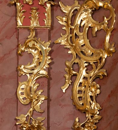 Zdjęcie nr 40: Nastawa ołtarzowa architektoniczna, jednokondygnacyjna ze zwieńczeniem, pięcioosiowa, ustawiona na wysokim cokole. Ołtarz wolnostojący, drewniany, sarkofagowy, wklęsło-wypukły, o zdwojonym froncie; mensa drewniana z marmurowym portatylem. Od frontu rocaille'owy kartusz ujęty fantazyjnymi płycinami oraz liśćmi. Na ołtarzu tabernakulum w formie sześcianu o wklęsłych bokach i wklęsło-wypukłym froncie; ujęte w narożach dwiema parami pilastrów o trzonach przechodzących w spływy wolutowe zdobione rocaille'm i różami. Pilastry podtrzymują falujący gzyms oraz fragmenty falistego, przerwanego, odwróconego przyczółka, przechodzącego w cokół, stanowiący tron wystawienia, na którym stoi krucyfiks. Na ściance frontowej obrotowa nisza, o wykroju stojącego prostokąta zamkniętego łukiem półkolistym, w opasce, zwieńczona kampanulami. W jej polu drzwiczki w formie stojącego prostokąta zamkniętego łukiem półkolistym w profilowanej ramie, z odlewanym przedstawieniem baranka leżącego na księdze z pieczęciami. Tabernakulum ujęte spływami przechodzącymi na krańcach we fragmenty wolutowego gzymsu, na których siedzą figury adorujących aniołów. Ponad tabernakulum fantazyjna ścianka tworząca tło dla tronu wystawienia z prześwitem otoczonym obłokami, z glorią promienistą, flankowana rocaille'owymi uszami. Cokół nastawy z wyodrębnionymi dwoma prostopadłościanami i dwoma konsolami, na dwóch skrajnych osiach bramki zamknięte wolutowymi szczytami tworzącymi cokoły dla figur, z przejściami w formie stojącego prostokąta zamkniętego łukiem odcinkowym nadwieszonym, z drzwiczkami. Cokół i drzwiczki dekorowane rocaille'm. Lico nastawy wklęsłe, osie wydzielone trzema parami pilastrów, na których tle stoją dwie pary kolumn o kapitelach kompozytowych. Podpory dźwigają pełne belkowanie, wyłamane na ich osi, przerwane nad polem środkowym, o gzymsie przechodzącym miejscami w rocaille'owe kartusze. Na osi środkowej wnęka z obrazem Matki Boskiej Wspomożenia Wiernych, w formie stojącego prostokąta zamkniętego łukiem odcinkowym nadwieszonym z uskokiem, ujęta profilowaną ramą, dekorowaną ponad łukiem płomienistym rocaille'm. Na pozostałych czterech osiach figury św. Barbary, św. Apolonii, św. Piotra i św. Pawła ustawione na rokokowych wspornikach. Trzony pilastrów i pola osi bocznych wypełnione rocaille'm, fryz dekorowany zwisami kwiatowymi. Zwieńczenie w formie zbliżonej do trapezu, zamknięte dwoma fragmentami gzymsu przechodzącego w woluty, flankowane wolutami spływającymi na belkowanie wewnętrznej pary kolumn, na których siedzą adorujące figury aniołów. W polu rzeźbiarska grupa Trójcy Świętej, pośród obłoków, w glorii promienistej, zwieńczona gołębicą Ducha Świętego w otoku z obłoków i uskrzydlonych główek anielskich, w glorii promienistej, flankowana przez dwa putta siedzące na gzymsie. Zwieńczenie po bokach obwiedzione rocaille'm, ujęte liśćmi palmowymi. Na belkowaniu, na osiach zewnętrznej pary kolumn wolutowe cokoły z rokokowymi wazonami. Struktura polichromowana na sposób imitujący marmoryzację w kolorze różowym i różowo-pomarańczowym, kolumny, profile i ornamentyka złocone, obłoki srebrzone. 

