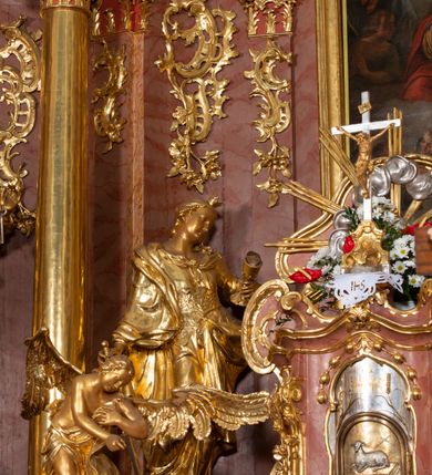 Zdjęcie nr 41: Nastawa ołtarzowa architektoniczna, jednokondygnacyjna ze zwieńczeniem, pięcioosiowa, ustawiona na wysokim cokole. Ołtarz wolnostojący, drewniany, sarkofagowy, wklęsło-wypukły, o zdwojonym froncie; mensa drewniana z marmurowym portatylem. Od frontu rocaille'owy kartusz ujęty fantazyjnymi płycinami oraz liśćmi. Na ołtarzu tabernakulum w formie sześcianu o wklęsłych bokach i wklęsło-wypukłym froncie; ujęte w narożach dwiema parami pilastrów o trzonach przechodzących w spływy wolutowe zdobione rocaille'm i różami. Pilastry podtrzymują falujący gzyms oraz fragmenty falistego, przerwanego, odwróconego przyczółka, przechodzącego w cokół, stanowiący tron wystawienia, na którym stoi krucyfiks. Na ściance frontowej obrotowa nisza, o wykroju stojącego prostokąta zamkniętego łukiem półkolistym, w opasce, zwieńczona kampanulami. W jej polu drzwiczki w formie stojącego prostokąta zamkniętego łukiem półkolistym w profilowanej ramie, z odlewanym przedstawieniem baranka leżącego na księdze z pieczęciami. Tabernakulum ujęte spływami przechodzącymi na krańcach we fragmenty wolutowego gzymsu, na których siedzą figury adorujących aniołów. Ponad tabernakulum fantazyjna ścianka tworząca tło dla tronu wystawienia z prześwitem otoczonym obłokami, z glorią promienistą, flankowana rocaille'owymi uszami. Cokół nastawy z wyodrębnionymi dwoma prostopadłościanami i dwoma konsolami, na dwóch skrajnych osiach bramki zamknięte wolutowymi szczytami tworzącymi cokoły dla figur, z przejściami w formie stojącego prostokąta zamkniętego łukiem odcinkowym nadwieszonym, z drzwiczkami. Cokół i drzwiczki dekorowane rocaille'm. Lico nastawy wklęsłe, osie wydzielone trzema parami pilastrów, na których tle stoją dwie pary kolumn o kapitelach kompozytowych. Podpory dźwigają pełne belkowanie, wyłamane na ich osi, przerwane nad polem środkowym, o gzymsie przechodzącym miejscami w rocaille'owe kartusze. Na osi środkowej wnęka z obrazem Matki Boskiej Wspomożenia Wiernych, w formie stojącego prostokąta zamkniętego łukiem odcinkowym nadwieszonym z uskokiem, ujęta profilowaną ramą, dekorowaną ponad łukiem płomienistym rocaille'm. Na pozostałych czterech osiach figury św. Barbary, św. Apolonii, św. Piotra i św. Pawła ustawione na rokokowych wspornikach. Trzony pilastrów i pola osi bocznych wypełnione rocaille'm, fryz dekorowany zwisami kwiatowymi. Zwieńczenie w formie zbliżonej do trapezu, zamknięte dwoma fragmentami gzymsu przechodzącego w woluty, flankowane wolutami spływającymi na belkowanie wewnętrznej pary kolumn, na których siedzą adorujące figury aniołów. W polu rzeźbiarska grupa Trójcy Świętej, pośród obłoków, w glorii promienistej, zwieńczona gołębicą Ducha Świętego w otoku z obłoków i uskrzydlonych główek anielskich, w glorii promienistej, flankowana przez dwa putta siedzące na gzymsie. Zwieńczenie po bokach obwiedzione rocaille'm, ujęte liśćmi palmowymi. Na belkowaniu, na osiach zewnętrznej pary kolumn wolutowe cokoły z rokokowymi wazonami. Struktura polichromowana na sposób imitujący marmoryzację w kolorze różowym i różowo-pomarańczowym, kolumny, profile i ornamentyka złocone, obłoki srebrzone. 

