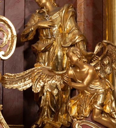 Zdjęcie nr 42: Nastawa ołtarzowa architektoniczna, jednokondygnacyjna ze zwieńczeniem, pięcioosiowa, ustawiona na wysokim cokole. Ołtarz wolnostojący, drewniany, sarkofagowy, wklęsło-wypukły, o zdwojonym froncie; mensa drewniana z marmurowym portatylem. Od frontu rocaille'owy kartusz ujęty fantazyjnymi płycinami oraz liśćmi. Na ołtarzu tabernakulum w formie sześcianu o wklęsłych bokach i wklęsło-wypukłym froncie; ujęte w narożach dwiema parami pilastrów o trzonach przechodzących w spływy wolutowe zdobione rocaille'm i różami. Pilastry podtrzymują falujący gzyms oraz fragmenty falistego, przerwanego, odwróconego przyczółka, przechodzącego w cokół, stanowiący tron wystawienia, na którym stoi krucyfiks. Na ściance frontowej obrotowa nisza, o wykroju stojącego prostokąta zamkniętego łukiem półkolistym, w opasce, zwieńczona kampanulami. W jej polu drzwiczki w formie stojącego prostokąta zamkniętego łukiem półkolistym w profilowanej ramie, z odlewanym przedstawieniem baranka leżącego na księdze z pieczęciami. Tabernakulum ujęte spływami przechodzącymi na krańcach we fragmenty wolutowego gzymsu, na których siedzą figury adorujących aniołów. Ponad tabernakulum fantazyjna ścianka tworząca tło dla tronu wystawienia z prześwitem otoczonym obłokami, z glorią promienistą, flankowana rocaille'owymi uszami. Cokół nastawy z wyodrębnionymi dwoma prostopadłościanami i dwoma konsolami, na dwóch skrajnych osiach bramki zamknięte wolutowymi szczytami tworzącymi cokoły dla figur, z przejściami w formie stojącego prostokąta zamkniętego łukiem odcinkowym nadwieszonym, z drzwiczkami. Cokół i drzwiczki dekorowane rocaille'm. Lico nastawy wklęsłe, osie wydzielone trzema parami pilastrów, na których tle stoją dwie pary kolumn o kapitelach kompozytowych. Podpory dźwigają pełne belkowanie, wyłamane na ich osi, przerwane nad polem środkowym, o gzymsie przechodzącym miejscami w rocaille'owe kartusze. Na osi środkowej wnęka z obrazem Matki Boskiej Wspomożenia Wiernych, w formie stojącego prostokąta zamkniętego łukiem odcinkowym nadwieszonym z uskokiem, ujęta profilowaną ramą, dekorowaną ponad łukiem płomienistym rocaille'm. Na pozostałych czterech osiach figury św. Barbary, św. Apolonii, św. Piotra i św. Pawła ustawione na rokokowych wspornikach. Trzony pilastrów i pola osi bocznych wypełnione rocaille'm, fryz dekorowany zwisami kwiatowymi. Zwieńczenie w formie zbliżonej do trapezu, zamknięte dwoma fragmentami gzymsu przechodzącego w woluty, flankowane wolutami spływającymi na belkowanie wewnętrznej pary kolumn, na których siedzą adorujące figury aniołów. W polu rzeźbiarska grupa Trójcy Świętej, pośród obłoków, w glorii promienistej, zwieńczona gołębicą Ducha Świętego w otoku z obłoków i uskrzydlonych główek anielskich, w glorii promienistej, flankowana przez dwa putta siedzące na gzymsie. Zwieńczenie po bokach obwiedzione rocaille'm, ujęte liśćmi palmowymi. Na belkowaniu, na osiach zewnętrznej pary kolumn wolutowe cokoły z rokokowymi wazonami. Struktura polichromowana na sposób imitujący marmoryzację w kolorze różowym i różowo-pomarańczowym, kolumny, profile i ornamentyka złocone, obłoki srebrzone. 

