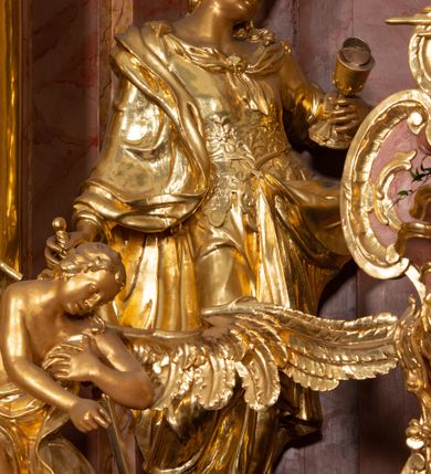 Zdjęcie nr 43: Nastawa ołtarzowa architektoniczna, jednokondygnacyjna ze zwieńczeniem, pięcioosiowa, ustawiona na wysokim cokole. Ołtarz wolnostojący, drewniany, sarkofagowy, wklęsło-wypukły, o zdwojonym froncie; mensa drewniana z marmurowym portatylem. Od frontu rocaille'owy kartusz ujęty fantazyjnymi płycinami oraz liśćmi. Na ołtarzu tabernakulum w formie sześcianu o wklęsłych bokach i wklęsło-wypukłym froncie; ujęte w narożach dwiema parami pilastrów o trzonach przechodzących w spływy wolutowe zdobione rocaille'm i różami. Pilastry podtrzymują falujący gzyms oraz fragmenty falistego, przerwanego, odwróconego przyczółka, przechodzącego w cokół, stanowiący tron wystawienia, na którym stoi krucyfiks. Na ściance frontowej obrotowa nisza, o wykroju stojącego prostokąta zamkniętego łukiem półkolistym, w opasce, zwieńczona kampanulami. W jej polu drzwiczki w formie stojącego prostokąta zamkniętego łukiem półkolistym w profilowanej ramie, z odlewanym przedstawieniem baranka leżącego na księdze z pieczęciami. Tabernakulum ujęte spływami przechodzącymi na krańcach we fragmenty wolutowego gzymsu, na których siedzą figury adorujących aniołów. Ponad tabernakulum fantazyjna ścianka tworząca tło dla tronu wystawienia z prześwitem otoczonym obłokami, z glorią promienistą, flankowana rocaille'owymi uszami. Cokół nastawy z wyodrębnionymi dwoma prostopadłościanami i dwoma konsolami, na dwóch skrajnych osiach bramki zamknięte wolutowymi szczytami tworzącymi cokoły dla figur, z przejściami w formie stojącego prostokąta zamkniętego łukiem odcinkowym nadwieszonym, z drzwiczkami. Cokół i drzwiczki dekorowane rocaille'm. Lico nastawy wklęsłe, osie wydzielone trzema parami pilastrów, na których tle stoją dwie pary kolumn o kapitelach kompozytowych. Podpory dźwigają pełne belkowanie, wyłamane na ich osi, przerwane nad polem środkowym, o gzymsie przechodzącym miejscami w rocaille'owe kartusze. Na osi środkowej wnęka z obrazem Matki Boskiej Wspomożenia Wiernych, w formie stojącego prostokąta zamkniętego łukiem odcinkowym nadwieszonym z uskokiem, ujęta profilowaną ramą, dekorowaną ponad łukiem płomienistym rocaille'm. Na pozostałych czterech osiach figury św. Barbary, św. Apolonii, św. Piotra i św. Pawła ustawione na rokokowych wspornikach. Trzony pilastrów i pola osi bocznych wypełnione rocaille'm, fryz dekorowany zwisami kwiatowymi. Zwieńczenie w formie zbliżonej do trapezu, zamknięte dwoma fragmentami gzymsu przechodzącego w woluty, flankowane wolutami spływającymi na belkowanie wewnętrznej pary kolumn, na których siedzą adorujące figury aniołów. W polu rzeźbiarska grupa Trójcy Świętej, pośród obłoków, w glorii promienistej, zwieńczona gołębicą Ducha Świętego w otoku z obłoków i uskrzydlonych główek anielskich, w glorii promienistej, flankowana przez dwa putta siedzące na gzymsie. Zwieńczenie po bokach obwiedzione rocaille'm, ujęte liśćmi palmowymi. Na belkowaniu, na osiach zewnętrznej pary kolumn wolutowe cokoły z rokokowymi wazonami. Struktura polichromowana na sposób imitujący marmoryzację w kolorze różowym i różowo-pomarańczowym, kolumny, profile i ornamentyka złocone, obłoki srebrzone. 

