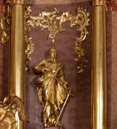 Zdjęcie nr 46: Nastawa ołtarzowa architektoniczna, jednokondygnacyjna ze zwieńczeniem, pięcioosiowa, ustawiona na wysokim cokole. Ołtarz wolnostojący, drewniany, sarkofagowy, wklęsło-wypukły, o zdwojonym froncie; mensa drewniana z marmurowym portatylem. Od frontu rocaille'owy kartusz ujęty fantazyjnymi płycinami oraz liśćmi. Na ołtarzu tabernakulum w formie sześcianu o wklęsłych bokach i wklęsło-wypukłym froncie; ujęte w narożach dwiema parami pilastrów o trzonach przechodzących w spływy wolutowe zdobione rocaille'm i różami. Pilastry podtrzymują falujący gzyms oraz fragmenty falistego, przerwanego, odwróconego przyczółka, przechodzącego w cokół, stanowiący tron wystawienia, na którym stoi krucyfiks. Na ściance frontowej obrotowa nisza, o wykroju stojącego prostokąta zamkniętego łukiem półkolistym, w opasce, zwieńczona kampanulami. W jej polu drzwiczki w formie stojącego prostokąta zamkniętego łukiem półkolistym w profilowanej ramie, z odlewanym przedstawieniem baranka leżącego na księdze z pieczęciami. Tabernakulum ujęte spływami przechodzącymi na krańcach we fragmenty wolutowego gzymsu, na których siedzą figury adorujących aniołów. Ponad tabernakulum fantazyjna ścianka tworząca tło dla tronu wystawienia z prześwitem otoczonym obłokami, z glorią promienistą, flankowana rocaille'owymi uszami. Cokół nastawy z wyodrębnionymi dwoma prostopadłościanami i dwoma konsolami, na dwóch skrajnych osiach bramki zamknięte wolutowymi szczytami tworzącymi cokoły dla figur, z przejściami w formie stojącego prostokąta zamkniętego łukiem odcinkowym nadwieszonym, z drzwiczkami. Cokół i drzwiczki dekorowane rocaille'm. Lico nastawy wklęsłe, osie wydzielone trzema parami pilastrów, na których tle stoją dwie pary kolumn o kapitelach kompozytowych. Podpory dźwigają pełne belkowanie, wyłamane na ich osi, przerwane nad polem środkowym, o gzymsie przechodzącym miejscami w rocaille'owe kartusze. Na osi środkowej wnęka z obrazem Matki Boskiej Wspomożenia Wiernych, w formie stojącego prostokąta zamkniętego łukiem odcinkowym nadwieszonym z uskokiem, ujęta profilowaną ramą, dekorowaną ponad łukiem płomienistym rocaille'm. Na pozostałych czterech osiach figury św. Barbary, św. Apolonii, św. Piotra i św. Pawła ustawione na rokokowych wspornikach. Trzony pilastrów i pola osi bocznych wypełnione rocaille'm, fryz dekorowany zwisami kwiatowymi. Zwieńczenie w formie zbliżonej do trapezu, zamknięte dwoma fragmentami gzymsu przechodzącego w woluty, flankowane wolutami spływającymi na belkowanie wewnętrznej pary kolumn, na których siedzą adorujące figury aniołów. W polu rzeźbiarska grupa Trójcy Świętej, pośród obłoków, w glorii promienistej, zwieńczona gołębicą Ducha Świętego w otoku z obłoków i uskrzydlonych główek anielskich, w glorii promienistej, flankowana przez dwa putta siedzące na gzymsie. Zwieńczenie po bokach obwiedzione rocaille'm, ujęte liśćmi palmowymi. Na belkowaniu, na osiach zewnętrznej pary kolumn wolutowe cokoły z rokokowymi wazonami. Struktura polichromowana na sposób imitujący marmoryzację w kolorze różowym i różowo-pomarańczowym, kolumny, profile i ornamentyka złocone, obłoki srebrzone. 

