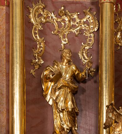 Zdjęcie nr 47: Nastawa ołtarzowa architektoniczna, jednokondygnacyjna ze zwieńczeniem, pięcioosiowa, ustawiona na wysokim cokole. Ołtarz wolnostojący, drewniany, sarkofagowy, wklęsło-wypukły, o zdwojonym froncie; mensa drewniana z marmurowym portatylem. Od frontu rocaille'owy kartusz ujęty fantazyjnymi płycinami oraz liśćmi. Na ołtarzu tabernakulum w formie sześcianu o wklęsłych bokach i wklęsło-wypukłym froncie; ujęte w narożach dwiema parami pilastrów o trzonach przechodzących w spływy wolutowe zdobione rocaille'm i różami. Pilastry podtrzymują falujący gzyms oraz fragmenty falistego, przerwanego, odwróconego przyczółka, przechodzącego w cokół, stanowiący tron wystawienia, na którym stoi krucyfiks. Na ściance frontowej obrotowa nisza, o wykroju stojącego prostokąta zamkniętego łukiem półkolistym, w opasce, zwieńczona kampanulami. W jej polu drzwiczki w formie stojącego prostokąta zamkniętego łukiem półkolistym w profilowanej ramie, z odlewanym przedstawieniem baranka leżącego na księdze z pieczęciami. Tabernakulum ujęte spływami przechodzącymi na krańcach we fragmenty wolutowego gzymsu, na których siedzą figury adorujących aniołów. Ponad tabernakulum fantazyjna ścianka tworząca tło dla tronu wystawienia z prześwitem otoczonym obłokami, z glorią promienistą, flankowana rocaille'owymi uszami. Cokół nastawy z wyodrębnionymi dwoma prostopadłościanami i dwoma konsolami, na dwóch skrajnych osiach bramki zamknięte wolutowymi szczytami tworzącymi cokoły dla figur, z przejściami w formie stojącego prostokąta zamkniętego łukiem odcinkowym nadwieszonym, z drzwiczkami. Cokół i drzwiczki dekorowane rocaille'm. Lico nastawy wklęsłe, osie wydzielone trzema parami pilastrów, na których tle stoją dwie pary kolumn o kapitelach kompozytowych. Podpory dźwigają pełne belkowanie, wyłamane na ich osi, przerwane nad polem środkowym, o gzymsie przechodzącym miejscami w rocaille'owe kartusze. Na osi środkowej wnęka z obrazem Matki Boskiej Wspomożenia Wiernych, w formie stojącego prostokąta zamkniętego łukiem odcinkowym nadwieszonym z uskokiem, ujęta profilowaną ramą, dekorowaną ponad łukiem płomienistym rocaille'm. Na pozostałych czterech osiach figury św. Barbary, św. Apolonii, św. Piotra i św. Pawła ustawione na rokokowych wspornikach. Trzony pilastrów i pola osi bocznych wypełnione rocaille'm, fryz dekorowany zwisami kwiatowymi. Zwieńczenie w formie zbliżonej do trapezu, zamknięte dwoma fragmentami gzymsu przechodzącego w woluty, flankowane wolutami spływającymi na belkowanie wewnętrznej pary kolumn, na których siedzą adorujące figury aniołów. W polu rzeźbiarska grupa Trójcy Świętej, pośród obłoków, w glorii promienistej, zwieńczona gołębicą Ducha Świętego w otoku z obłoków i uskrzydlonych główek anielskich, w glorii promienistej, flankowana przez dwa putta siedzące na gzymsie. Zwieńczenie po bokach obwiedzione rocaille'm, ujęte liśćmi palmowymi. Na belkowaniu, na osiach zewnętrznej pary kolumn wolutowe cokoły z rokokowymi wazonami. Struktura polichromowana na sposób imitujący marmoryzację w kolorze różowym i różowo-pomarańczowym, kolumny, profile i ornamentyka złocone, obłoki srebrzone. 

