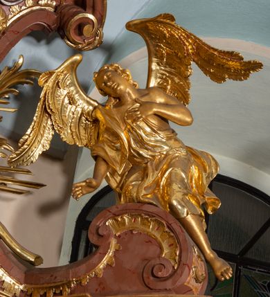 Zdjęcie nr 48: Nastawa ołtarzowa architektoniczna, jednokondygnacyjna ze zwieńczeniem, pięcioosiowa, ustawiona na wysokim cokole. Ołtarz wolnostojący, drewniany, sarkofagowy, wklęsło-wypukły, o zdwojonym froncie; mensa drewniana z marmurowym portatylem. Od frontu rocaille&#039;owy kartusz ujęty fantazyjnymi płycinami oraz liśćmi. Na ołtarzu tabernakulum w formie sześcianu o wklęsłych bokach i wklęsło-wypukłym froncie; ujęte w narożach dwiema parami pilastrów o trzonach przechodzących w spływy wolutowe zdobione rocaille&#039;m i różami. Pilastry podtrzymują falujący gzyms oraz fragmenty falistego, przerwanego, odwróconego przyczółka, przechodzącego w cokół, stanowiący tron wystawienia, na którym stoi krucyfiks. Na ściance frontowej obrotowa nisza, o wykroju stojącego prostokąta zamkniętego łukiem półkolistym, w opasce, zwieńczona kampanulami. W jej polu drzwiczki w formie stojącego prostokąta zamkniętego łukiem półkolistym w profilowanej ramie, z odlewanym przedstawieniem baranka leżącego na księdze z pieczęciami. Tabernakulum ujęte spływami przechodzącymi na krańcach we fragmenty wolutowego gzymsu, na których siedzą figury adorujących aniołów. Ponad tabernakulum fantazyjna ścianka tworząca tło dla tronu wystawienia z prześwitem otoczonym obłokami, z glorią promienistą, flankowana rocaille&#039;owymi uszami. Cokół nastawy z wyodrębnionymi dwoma prostopadłościanami i dwoma konsolami, na dwóch skrajnych osiach bramki zamknięte wolutowymi szczytami tworzącymi cokoły dla figur, z przejściami w formie stojącego prostokąta zamkniętego łukiem odcinkowym nadwieszonym, z drzwiczkami. Cokół i drzwiczki dekorowane rocaille&#039;m. Lico nastawy wklęsłe, osie wydzielone trzema parami pilastrów, na których tle stoją dwie pary kolumn o kapitelach kompozytowych. Podpory dźwigają pełne belkowanie, wyłamane na ich osi, przerwane nad polem środkowym, o gzymsie przechodzącym miejscami w rocaille&#039;owe kartusze. Na osi środkowej wnęka z obrazem Matki Boskiej Wspomożenia Wiernych, w formie stojącego prostokąta zamkniętego łukiem odcinkowym nadwieszonym z uskokiem, ujęta profilowaną ramą, dekorowaną ponad łukiem płomienistym rocaille&#039;m. Na pozostałych czterech osiach figury św. Barbary, św. Apolonii, św. Piotra i św. Pawła ustawione na rokokowych wspornikach. Trzony pilastrów i pola osi bocznych wypełnione rocaille&#039;m, fryz dekorowany zwisami kwiatowymi. Zwieńczenie w formie zbliżonej do trapezu, zamknięte dwoma fragmentami gzymsu przechodzącego w woluty, flankowane wolutami spływającymi na belkowanie wewnętrznej pary kolumn, na których siedzą adorujące figury aniołów. W polu rzeźbiarska grupa Trójcy Świętej, pośród obłoków, w glorii promienistej, zwieńczona gołębicą Ducha Świętego w otoku z obłoków i uskrzydlonych główek anielskich, w glorii promienistej, flankowana przez dwa putta siedzące na gzymsie. Zwieńczenie po bokach obwiedzione rocaille&#039;m, ujęte liśćmi palmowymi. Na belkowaniu, na osiach zewnętrznej pary kolumn wolutowe cokoły z rokokowymi wazonami. Struktura polichromowana na sposób imitujący marmoryzację w kolorze różowym i różowo-pomarańczowym, kolumny, profile i ornamentyka złocone, obłoki srebrzone. 

