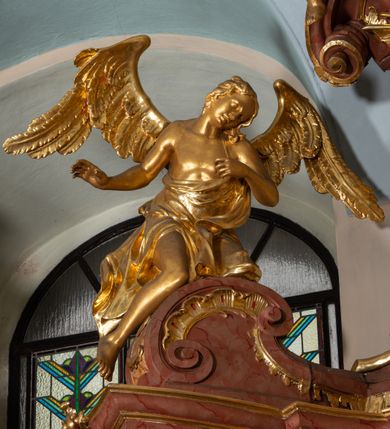 Zdjęcie nr 49: Nastawa ołtarzowa architektoniczna, jednokondygnacyjna ze zwieńczeniem, pięcioosiowa, ustawiona na wysokim cokole. Ołtarz wolnostojący, drewniany, sarkofagowy, wklęsło-wypukły, o zdwojonym froncie; mensa drewniana z marmurowym portatylem. Od frontu rocaille'owy kartusz ujęty fantazyjnymi płycinami oraz liśćmi. Na ołtarzu tabernakulum w formie sześcianu o wklęsłych bokach i wklęsło-wypukłym froncie; ujęte w narożach dwiema parami pilastrów o trzonach przechodzących w spływy wolutowe zdobione rocaille'm i różami. Pilastry podtrzymują falujący gzyms oraz fragmenty falistego, przerwanego, odwróconego przyczółka, przechodzącego w cokół, stanowiący tron wystawienia, na którym stoi krucyfiks. Na ściance frontowej obrotowa nisza, o wykroju stojącego prostokąta zamkniętego łukiem półkolistym, w opasce, zwieńczona kampanulami. W jej polu drzwiczki w formie stojącego prostokąta zamkniętego łukiem półkolistym w profilowanej ramie, z odlewanym przedstawieniem baranka leżącego na księdze z pieczęciami. Tabernakulum ujęte spływami przechodzącymi na krańcach we fragmenty wolutowego gzymsu, na których siedzą figury adorujących aniołów. Ponad tabernakulum fantazyjna ścianka tworząca tło dla tronu wystawienia z prześwitem otoczonym obłokami, z glorią promienistą, flankowana rocaille'owymi uszami. Cokół nastawy z wyodrębnionymi dwoma prostopadłościanami i dwoma konsolami, na dwóch skrajnych osiach bramki zamknięte wolutowymi szczytami tworzącymi cokoły dla figur, z przejściami w formie stojącego prostokąta zamkniętego łukiem odcinkowym nadwieszonym, z drzwiczkami. Cokół i drzwiczki dekorowane rocaille'm. Lico nastawy wklęsłe, osie wydzielone trzema parami pilastrów, na których tle stoją dwie pary kolumn o kapitelach kompozytowych. Podpory dźwigają pełne belkowanie, wyłamane na ich osi, przerwane nad polem środkowym, o gzymsie przechodzącym miejscami w rocaille'owe kartusze. Na osi środkowej wnęka z obrazem Matki Boskiej Wspomożenia Wiernych, w formie stojącego prostokąta zamkniętego łukiem odcinkowym nadwieszonym z uskokiem, ujęta profilowaną ramą, dekorowaną ponad łukiem płomienistym rocaille'm. Na pozostałych czterech osiach figury św. Barbary, św. Apolonii, św. Piotra i św. Pawła ustawione na rokokowych wspornikach. Trzony pilastrów i pola osi bocznych wypełnione rocaille'm, fryz dekorowany zwisami kwiatowymi. Zwieńczenie w formie zbliżonej do trapezu, zamknięte dwoma fragmentami gzymsu przechodzącego w woluty, flankowane wolutami spływającymi na belkowanie wewnętrznej pary kolumn, na których siedzą adorujące figury aniołów. W polu rzeźbiarska grupa Trójcy Świętej, pośród obłoków, w glorii promienistej, zwieńczona gołębicą Ducha Świętego w otoku z obłoków i uskrzydlonych główek anielskich, w glorii promienistej, flankowana przez dwa putta siedzące na gzymsie. Zwieńczenie po bokach obwiedzione rocaille'm, ujęte liśćmi palmowymi. Na belkowaniu, na osiach zewnętrznej pary kolumn wolutowe cokoły z rokokowymi wazonami. Struktura polichromowana na sposób imitujący marmoryzację w kolorze różowym i różowo-pomarańczowym, kolumny, profile i ornamentyka złocone, obłoki srebrzone. 

