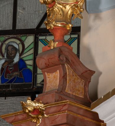 Zdjęcie nr 50: Nastawa ołtarzowa architektoniczna, jednokondygnacyjna ze zwieńczeniem, pięcioosiowa, ustawiona na wysokim cokole. Ołtarz wolnostojący, drewniany, sarkofagowy, wklęsło-wypukły, o zdwojonym froncie; mensa drewniana z marmurowym portatylem. Od frontu rocaille'owy kartusz ujęty fantazyjnymi płycinami oraz liśćmi. Na ołtarzu tabernakulum w formie sześcianu o wklęsłych bokach i wklęsło-wypukłym froncie; ujęte w narożach dwiema parami pilastrów o trzonach przechodzących w spływy wolutowe zdobione rocaille'm i różami. Pilastry podtrzymują falujący gzyms oraz fragmenty falistego, przerwanego, odwróconego przyczółka, przechodzącego w cokół, stanowiący tron wystawienia, na którym stoi krucyfiks. Na ściance frontowej obrotowa nisza, o wykroju stojącego prostokąta zamkniętego łukiem półkolistym, w opasce, zwieńczona kampanulami. W jej polu drzwiczki w formie stojącego prostokąta zamkniętego łukiem półkolistym w profilowanej ramie, z odlewanym przedstawieniem baranka leżącego na księdze z pieczęciami. Tabernakulum ujęte spływami przechodzącymi na krańcach we fragmenty wolutowego gzymsu, na których siedzą figury adorujących aniołów. Ponad tabernakulum fantazyjna ścianka tworząca tło dla tronu wystawienia z prześwitem otoczonym obłokami, z glorią promienistą, flankowana rocaille'owymi uszami. Cokół nastawy z wyodrębnionymi dwoma prostopadłościanami i dwoma konsolami, na dwóch skrajnych osiach bramki zamknięte wolutowymi szczytami tworzącymi cokoły dla figur, z przejściami w formie stojącego prostokąta zamkniętego łukiem odcinkowym nadwieszonym, z drzwiczkami. Cokół i drzwiczki dekorowane rocaille'm. Lico nastawy wklęsłe, osie wydzielone trzema parami pilastrów, na których tle stoją dwie pary kolumn o kapitelach kompozytowych. Podpory dźwigają pełne belkowanie, wyłamane na ich osi, przerwane nad polem środkowym, o gzymsie przechodzącym miejscami w rocaille'owe kartusze. Na osi środkowej wnęka z obrazem Matki Boskiej Wspomożenia Wiernych, w formie stojącego prostokąta zamkniętego łukiem odcinkowym nadwieszonym z uskokiem, ujęta profilowaną ramą, dekorowaną ponad łukiem płomienistym rocaille'm. Na pozostałych czterech osiach figury św. Barbary, św. Apolonii, św. Piotra i św. Pawła ustawione na rokokowych wspornikach. Trzony pilastrów i pola osi bocznych wypełnione rocaille'm, fryz dekorowany zwisami kwiatowymi. Zwieńczenie w formie zbliżonej do trapezu, zamknięte dwoma fragmentami gzymsu przechodzącego w woluty, flankowane wolutami spływającymi na belkowanie wewnętrznej pary kolumn, na których siedzą adorujące figury aniołów. W polu rzeźbiarska grupa Trójcy Świętej, pośród obłoków, w glorii promienistej, zwieńczona gołębicą Ducha Świętego w otoku z obłoków i uskrzydlonych główek anielskich, w glorii promienistej, flankowana przez dwa putta siedzące na gzymsie. Zwieńczenie po bokach obwiedzione rocaille'm, ujęte liśćmi palmowymi. Na belkowaniu, na osiach zewnętrznej pary kolumn wolutowe cokoły z rokokowymi wazonami. Struktura polichromowana na sposób imitujący marmoryzację w kolorze różowym i różowo-pomarańczowym, kolumny, profile i ornamentyka złocone, obłoki srebrzone. 

