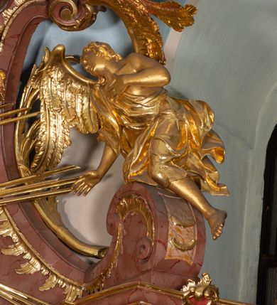 Zdjęcie nr 53: Nastawa ołtarzowa architektoniczna, jednokondygnacyjna ze zwieńczeniem, pięcioosiowa, ustawiona na wysokim cokole. Ołtarz wolnostojący, drewniany, sarkofagowy, wklęsło-wypukły, o zdwojonym froncie; mensa drewniana z marmurowym portatylem. Od frontu rocaille'owy kartusz ujęty fantazyjnymi płycinami oraz liśćmi. Na ołtarzu tabernakulum w formie sześcianu o wklęsłych bokach i wklęsło-wypukłym froncie; ujęte w narożach dwiema parami pilastrów o trzonach przechodzących w spływy wolutowe zdobione rocaille'm i różami. Pilastry podtrzymują falujący gzyms oraz fragmenty falistego, przerwanego, odwróconego przyczółka, przechodzącego w cokół, stanowiący tron wystawienia, na którym stoi krucyfiks. Na ściance frontowej obrotowa nisza, o wykroju stojącego prostokąta zamkniętego łukiem półkolistym, w opasce, zwieńczona kampanulami. W jej polu drzwiczki w formie stojącego prostokąta zamkniętego łukiem półkolistym w profilowanej ramie, z odlewanym przedstawieniem baranka leżącego na księdze z pieczęciami. Tabernakulum ujęte spływami przechodzącymi na krańcach we fragmenty wolutowego gzymsu, na których siedzą figury adorujących aniołów. Ponad tabernakulum fantazyjna ścianka tworząca tło dla tronu wystawienia z prześwitem otoczonym obłokami, z glorią promienistą, flankowana rocaille'owymi uszami. Cokół nastawy z wyodrębnionymi dwoma prostopadłościanami i dwoma konsolami, na dwóch skrajnych osiach bramki zamknięte wolutowymi szczytami tworzącymi cokoły dla figur, z przejściami w formie stojącego prostokąta zamkniętego łukiem odcinkowym nadwieszonym, z drzwiczkami. Cokół i drzwiczki dekorowane rocaille'm. Lico nastawy wklęsłe, osie wydzielone trzema parami pilastrów, na których tle stoją dwie pary kolumn o kapitelach kompozytowych. Podpory dźwigają pełne belkowanie, wyłamane na ich osi, przerwane nad polem środkowym, o gzymsie przechodzącym miejscami w rocaille'owe kartusze. Na osi środkowej wnęka z obrazem Matki Boskiej Wspomożenia Wiernych, w formie stojącego prostokąta zamkniętego łukiem odcinkowym nadwieszonym z uskokiem, ujęta profilowaną ramą, dekorowaną ponad łukiem płomienistym rocaille'm. Na pozostałych czterech osiach figury św. Barbary, św. Apolonii, św. Piotra i św. Pawła ustawione na rokokowych wspornikach. Trzony pilastrów i pola osi bocznych wypełnione rocaille'm, fryz dekorowany zwisami kwiatowymi. Zwieńczenie w formie zbliżonej do trapezu, zamknięte dwoma fragmentami gzymsu przechodzącego w woluty, flankowane wolutami spływającymi na belkowanie wewnętrznej pary kolumn, na których siedzą adorujące figury aniołów. W polu rzeźbiarska grupa Trójcy Świętej, pośród obłoków, w glorii promienistej, zwieńczona gołębicą Ducha Świętego w otoku z obłoków i uskrzydlonych główek anielskich, w glorii promienistej, flankowana przez dwa putta siedzące na gzymsie. Zwieńczenie po bokach obwiedzione rocaille'm, ujęte liśćmi palmowymi. Na belkowaniu, na osiach zewnętrznej pary kolumn wolutowe cokoły z rokokowymi wazonami. Struktura polichromowana na sposób imitujący marmoryzację w kolorze różowym i różowo-pomarańczowym, kolumny, profile i ornamentyka złocone, obłoki srebrzone. 

