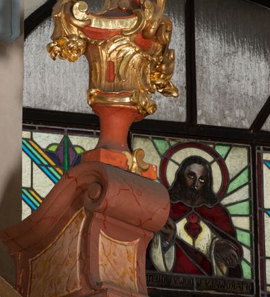 Zdjęcie nr 51: Nastawa ołtarzowa architektoniczna, jednokondygnacyjna ze zwieńczeniem, pięcioosiowa, ustawiona na wysokim cokole. Ołtarz wolnostojący, drewniany, sarkofagowy, wklęsło-wypukły, o zdwojonym froncie; mensa drewniana z marmurowym portatylem. Od frontu rocaille'owy kartusz ujęty fantazyjnymi płycinami oraz liśćmi. Na ołtarzu tabernakulum w formie sześcianu o wklęsłych bokach i wklęsło-wypukłym froncie; ujęte w narożach dwiema parami pilastrów o trzonach przechodzących w spływy wolutowe zdobione rocaille'm i różami. Pilastry podtrzymują falujący gzyms oraz fragmenty falistego, przerwanego, odwróconego przyczółka, przechodzącego w cokół, stanowiący tron wystawienia, na którym stoi krucyfiks. Na ściance frontowej obrotowa nisza, o wykroju stojącego prostokąta zamkniętego łukiem półkolistym, w opasce, zwieńczona kampanulami. W jej polu drzwiczki w formie stojącego prostokąta zamkniętego łukiem półkolistym w profilowanej ramie, z odlewanym przedstawieniem baranka leżącego na księdze z pieczęciami. Tabernakulum ujęte spływami przechodzącymi na krańcach we fragmenty wolutowego gzymsu, na których siedzą figury adorujących aniołów. Ponad tabernakulum fantazyjna ścianka tworząca tło dla tronu wystawienia z prześwitem otoczonym obłokami, z glorią promienistą, flankowana rocaille'owymi uszami. Cokół nastawy z wyodrębnionymi dwoma prostopadłościanami i dwoma konsolami, na dwóch skrajnych osiach bramki zamknięte wolutowymi szczytami tworzącymi cokoły dla figur, z przejściami w formie stojącego prostokąta zamkniętego łukiem odcinkowym nadwieszonym, z drzwiczkami. Cokół i drzwiczki dekorowane rocaille'm. Lico nastawy wklęsłe, osie wydzielone trzema parami pilastrów, na których tle stoją dwie pary kolumn o kapitelach kompozytowych. Podpory dźwigają pełne belkowanie, wyłamane na ich osi, przerwane nad polem środkowym, o gzymsie przechodzącym miejscami w rocaille'owe kartusze. Na osi środkowej wnęka z obrazem Matki Boskiej Wspomożenia Wiernych, w formie stojącego prostokąta zamkniętego łukiem odcinkowym nadwieszonym z uskokiem, ujęta profilowaną ramą, dekorowaną ponad łukiem płomienistym rocaille'm. Na pozostałych czterech osiach figury św. Barbary, św. Apolonii, św. Piotra i św. Pawła ustawione na rokokowych wspornikach. Trzony pilastrów i pola osi bocznych wypełnione rocaille'm, fryz dekorowany zwisami kwiatowymi. Zwieńczenie w formie zbliżonej do trapezu, zamknięte dwoma fragmentami gzymsu przechodzącego w woluty, flankowane wolutami spływającymi na belkowanie wewnętrznej pary kolumn, na których siedzą adorujące figury aniołów. W polu rzeźbiarska grupa Trójcy Świętej, pośród obłoków, w glorii promienistej, zwieńczona gołębicą Ducha Świętego w otoku z obłoków i uskrzydlonych główek anielskich, w glorii promienistej, flankowana przez dwa putta siedzące na gzymsie. Zwieńczenie po bokach obwiedzione rocaille'm, ujęte liśćmi palmowymi. Na belkowaniu, na osiach zewnętrznej pary kolumn wolutowe cokoły z rokokowymi wazonami. Struktura polichromowana na sposób imitujący marmoryzację w kolorze różowym i różowo-pomarańczowym, kolumny, profile i ornamentyka złocone, obłoki srebrzone. 

