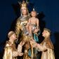 Zdjęcie nr 1: Grupa rzeźbiarska przedstawiająca stojącą Matkę Boską z Dzieciątkiem, przed którą klęczą święci. W centrum figura Marii, ustawiona na cokole, ukazana frontalnie, w całej postaci, z głową skierowaną w prawo. Lewą ręką podtrzymuje Dzieciątko, prawą wyciąga w stronę św. Dominika. Twarz ma pociągłą, o migdałowatych oczach, prostym nosie i wąskich ustach, okoloną brązowymi włosami. Ubrana jest w złoconą tunikę i złocony płaszcz o niebieskiej podszewce, zarzucony na głowę i opasujący postać. Na głowie ma otwartą koronę. Dzieciątko w pozycji siedzącej, zwrócone w trzech czwartych w prawo, z głową ukazaną frontalnie, w prawej ręce trzyma jabłko królewskie, lewą wyciąga w stronę św. Katarzyny. Twarz ma kwadratową, o wąskich oczach, krótkim nosie i małych ustach, okoloną jasnobrązowymi, krótkimi włosami. Z jego głowy odchodzą trzy wiązki promieni. W partii bioder przewiązane jest srebrzoną pieluszką. Po prawej stronie Marii klęczy św. Dominik, ukazany z profilu, z uniesioną głową i wyciągniętymi przed siebie rękami. Twarz ma szczupłą, o migdałowatych oczach, prostym nosie i małych ustach, okoloną krótkimi włosami, z tonsurą na głowie. Ubrany jest w biały habit, ze złoconą pelerynką, szkaplerzem oraz płaszczem. Po lewej stronie Marii klęczy św. Katarzyna, ukazana z profilu, z uniesioną głową i wyciągniętymi przed siebie rękami. Twarz ma szczupłą, o migdałowatych oczach, prostym nosie i małych ustach. Ubrana jest w biały habit, ze złoconą pelerynką, szkaplerzem, welonem i płaszczem. Na głowie ma koronę cierniową. Polichromia ciał postaci naturalistyczna. 

