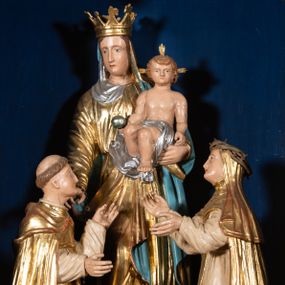 Zdjęcie nr 1: Grupa rzeźbiarska przedstawiająca stojącą Matkę Boską z Dzieciątkiem, przed którą klęczą święci. W centrum figura Marii, ustawiona na cokole, ukazana frontalnie, w całej postaci, z głową skierowaną w prawo. Lewą ręką podtrzymuje Dzieciątko, prawą wyciąga w stronę św. Dominika. Twarz ma pociągłą, o migdałowatych oczach, prostym nosie i wąskich ustach, okoloną brązowymi włosami. Ubrana jest w złoconą tunikę i złocony płaszcz o niebieskiej podszewce, zarzucony na głowę i opasujący postać. Na głowie ma otwartą koronę. Dzieciątko w pozycji siedzącej, zwrócone w trzech czwartych w prawo, z głową ukazaną frontalnie, w prawej ręce trzyma jabłko królewskie, lewą wyciąga w stronę św. Katarzyny. Twarz ma kwadratową, o wąskich oczach, krótkim nosie i małych ustach, okoloną jasnobrązowymi, krótkimi włosami. Z jego głowy odchodzą trzy wiązki promieni. W partii bioder przewiązane jest srebrzoną pieluszką. Po prawej stronie Marii klęczy św. Dominik, ukazany z profilu, z uniesioną głową i wyciągniętymi przed siebie rękami. Twarz ma szczupłą, o migdałowatych oczach, prostym nosie i małych ustach, okoloną krótkimi włosami, z tonsurą na głowie. Ubrany jest w biały habit, ze złoconą pelerynką, szkaplerzem oraz płaszczem. Po lewej stronie Marii klęczy św. Katarzyna, ukazana z profilu, z uniesioną głową i wyciągniętymi przed siebie rękami. Twarz ma szczupłą, o migdałowatych oczach, prostym nosie i małych ustach. Ubrana jest w biały habit, ze złoconą pelerynką, szkaplerzem, welonem i płaszczem. Na głowie ma koronę cierniową. Polichromia ciał postaci naturalistyczna. 

