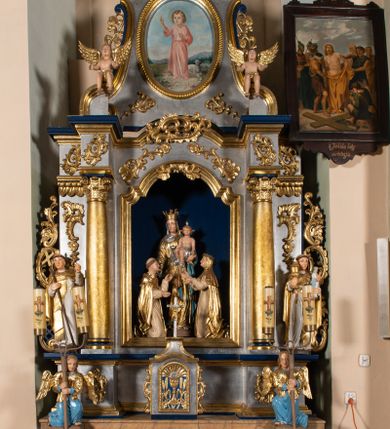 Zdjęcie nr 1: Nastawa architektoniczna, jednoosiowa, jednokondygnacyjna ze zwieńczeniem. Ołtarz sarkofagowy, wklęsło-wypukły, na cokole, z drewnianą mensą. Na ołtarzu tabernakulum w formie drewnianej skrzynki, obwiedzionej gzymsem i zwieńczonej cokołem z krzyżem. Drzwiczki w kształcie stojącego prostokąta zamkniętego łukiem odcinkowym nadwieszonym, w opasce, z płaskorzeźbionym przedstawieniem kielicha z hostią w glorii pomiędzy kłosami zbóż. Na ołtarzu dwie figury klęczących aniołów trzymających świeczniki. 
Nastawa ustawiona na cokole z wyodrębnionymi dwoma prostopadłościanami, ujęta parą kolumn podtrzymujących belkowanie, częściowo przerwane nad polem środkowym, o gzymsie wyłamanym na kształt łuku odcinkowego. Na belkowaniu fragmenty przerwanego, półkolistego przyczółka z siedzącą parą aniołków. W polu środkowym wnęka w formie stojącego prostokąta zamkniętego łukiem półkolistym nadwieszonym, z uskokiem, ujęta profilowaną ramą, z grupą rzeźbiarską Matki Boskiej Różańcowej ze św. Dominikiem i św. Katarzyną Sieneńską. Po zewnętrznej stronie kolumn ustawione figury św. Jacka i bł. Czesława. Wszystkie pola nastawy wypełnione stylizowanym rocaille'm, uszy utworzone z rocaille'u. Zwieńczenie w formie zbliżonej do trapezu, ujęte spływami wolutowymi, zamknięte dwoma fragmentami wolutowego gzymsu. W polu obraz w formie stojącego owalu, ujęty ramą, z przedstawieniem Dzieciątka Jezus. Zwieńczenie flankowane uszami utworzonymi z winnej latorośli. Całość zakończona rzeźbioną gołębicą Ducha Świętego w glorii promienistej. Struktura ołtarza polichromowana na srebrno, z niebieskimi elementami, złoconymi kolumnami, profilami i ornamentyką. 


