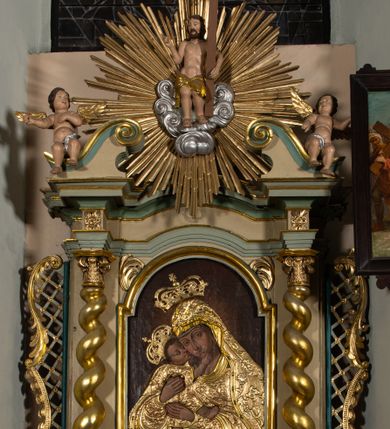 Zdjęcie nr 1: Nastawa architektoniczna, jednokondygnacyjna, jednoosiowa, ustawiona na cokole z wyodrębnionymi prostopadłościanami. Ołtarz drewniany, sarkofagowy, na cokole, z drewnianą mensą i kamiennym portatylem. Cokół nastawy dekorowany płycinami z akantem. Retabulum ujęte parą kolumn o skręconych trzonach i korynckich kapitelach, dźwigających pełne belkowanie, nad polem środkowym wyłamane na kształt łuku odcinkowego. Na belkowaniu fragmenty falistego, przerwanego przyczółka z siedzącymi puttami. Całe pole środkowe wypełnione wnęką w formie stojącego prostokąta zamkniętego łukiem półkolistym nadwieszonym, ujętą profilowaną ramą, z obrazem Matki Boskiej Wspomożenia Wiernych. Nastawa flankowana uszami utworzonymi z akantu i kratki regencyjnej. W miejscu zwieńczenia figura siedzącego na obłoku Chrystusa trzymającego krzyż, w glorii promienistej. Struktura polichromowana w kolorze beżowym, z jasnoniebieskimi i niebieskimi detalami, złoconymi kolumnami, profilami i ornamentyką oraz srebrzonymi detalami. 
