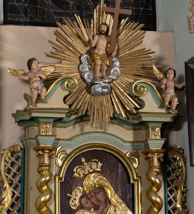 Zdjęcie nr 5: Nastawa architektoniczna, jednokondygnacyjna, jednoosiowa, ustawiona na cokole z wyodrębnionymi prostopadłościanami. Ołtarz drewniany, sarkofagowy, na cokole, z drewnianą mensą i kamiennym portatylem. Cokół nastawy dekorowany płycinami z akantem. Retabulum ujęte parą kolumn o skręconych trzonach i korynckich kapitelach, dźwigających pełne belkowanie, nad polem środkowym wyłamane na kształt łuku odcinkowego. Na belkowaniu fragmenty falistego, przerwanego przyczółka z siedzącymi puttami. Całe pole środkowe wypełnione wnęką w formie stojącego prostokąta zamkniętego łukiem półkolistym nadwieszonym, ujętą profilowaną ramą, z obrazem Matki Boskiej Wspomożenia Wiernych. Nastawa flankowana uszami utworzonymi z akantu i kratki regencyjnej. W miejscu zwieńczenia figura siedzącego na obłoku Chrystusa trzymającego krzyż, w glorii promienistej. Struktura polichromowana w kolorze beżowym, z jasnoniebieskimi i niebieskimi detalami, złoconymi kolumnami, profilami i ornamentyką oraz srebrzonymi detalami. 
