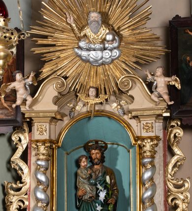 Zdjęcie nr 1: Nastawa architektoniczna, jednokondygnacyjna, jednoosiowa, ustawiona na cokole z wyodrębnionymi prostopadłościanami. Ołtarz drewniany, sarkofagowy, na cokole, z drewnianą mensą i kamiennym portatylem. Na ołtarzu ustawiony postument, ujęty spływami wolutowymi, dekorowany z przodu akantem i muszlą. Cokół nastawy dekorowany płycinami z uskrzydlonymi główkami anielskimi. Retabulum ujęte parą kolumn o skręconych trzonach i korynckich kapitelach, dźwigających niepełne belkowanie, częściowo przerwane nad polem środkowym, na którym gzyms wyłamany jest na kształt łuku odcinkowego. Na belkowaniu fragmenty falistego, przerwanego przyczółka z siedzącymi puttami. Całe pole środkowe wypełnione niszą w formie stojącego prostokąta zamkniętego łukiem półkolistym nadwieszonym, ujętą profilowaną ramą, z figurą św. Józefa z Dzieciątkiem. Nad niszą uskrzydlona główka anielska i dwie kiści winogron. Nastawa flankowana uszami utworzonymi z akantu i wstęgi regencyjnej. W miejscu zwieńczenia płaskorzeźbiona półpostać Boga Ojca pośród obłoków, w glorii promienistej. Struktura polichromowana w kolorze beżowym, z jasnoróżowymi detalami, srebrzonymi trzonami kolumn oraz złoconymi profilami i ornamentyką. 
