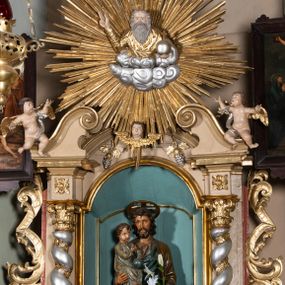 Zdjęcie nr 1: Nastawa architektoniczna, jednokondygnacyjna, jednoosiowa, ustawiona na cokole z wyodrębnionymi prostopadłościanami. Ołtarz drewniany, sarkofagowy, na cokole, z drewnianą mensą i kamiennym portatylem. Na ołtarzu ustawiony postument, ujęty spływami wolutowymi, dekorowany z przodu akantem i muszlą. Cokół nastawy dekorowany płycinami z uskrzydlonymi główkami anielskimi. Retabulum ujęte parą kolumn o skręconych trzonach i korynckich kapitelach, dźwigających niepełne belkowanie, częściowo przerwane nad polem środkowym, na którym gzyms wyłamany jest na kształt łuku odcinkowego. Na belkowaniu fragmenty falistego, przerwanego przyczółka z siedzącymi puttami. Całe pole środkowe wypełnione niszą w formie stojącego prostokąta zamkniętego łukiem półkolistym nadwieszonym, ujętą profilowaną ramą, z figurą św. Józefa z Dzieciątkiem. Nad niszą uskrzydlona główka anielska i dwie kiści winogron. Nastawa flankowana uszami utworzonymi z akantu i wstęgi regencyjnej. W miejscu zwieńczenia płaskorzeźbiona półpostać Boga Ojca pośród obłoków, w glorii promienistej. Struktura polichromowana w kolorze beżowym, z jasnoróżowymi detalami, srebrzonymi trzonami kolumn oraz złoconymi profilami i ornamentyką. 
