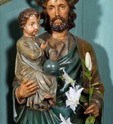Zdjęcie nr 3: Rzeźba pełnoplastyczna, ustawiona na niskim, ośmiobocznym postumencie. Święty ukazany w całej postaci, frontalnie, w kontrapoście, prawą ręką podtrzymuje na ramieniu Dzieciątko, w lewej, ugiętej trzyma gałązkę lilii. Twarz ma szczupłą, pociągłą, o małych, migdałowatych oczach, prostym nosie i małych ustach, okoloną krótką brodą oraz kręconymi, brązowymi włosami. Nad głową nimb. Ubrany jest w lejącą szaro-brązową tunikę oraz brązowo-zielony płaszcz z niebieską podszewką, lamowany złoconą dekoracją roślinną, zarzucony na ramiona i zawinięty wokół ciała. Dzieciątko w pozycji siedzącej, zwrócone w trzech czwartych w lewo, prawą ręką wskazuje na Józefa, lewą przytrzymuje na kolanach kulę. Twarz ma pociągłą, o pełnych policzkach, dużych, migdałowatych oczach, małym nosie i ustach, okoloną krótkimi, brązowymi włosami. Ubrane jest w luźną jasnoniebieską tunikę pokrytą złoconymi gwiazdami, ze złoconą lamówką. Polichromia ciał naturalistyczna. 


