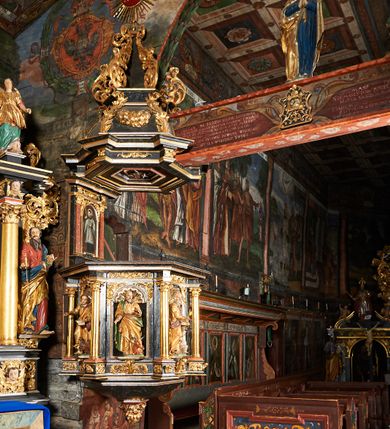 Zdjęcie nr 3: Ambona przyścienna, wisząca, ustawiona na północnym węgarze arkady tęczowej, dostępna przez schody od strony zakrystii. Kosz na planie sześcioboku z wysuniętą w stronę ołtarza częścią prowadzącą do drzwi. Ścianki wydzielone kolumnami o kapitelach korynckich, ustawionymi na postumentach, podtrzymującymi parapet z silnie wysuniętym gzymsem. Między kolumnami płytkie nisze zwieńczone konchami z figurami czterech ewangelistów i Chrystusa. Przyłucza, fryz i cokół dekorowany akantem. Kosz u spodu z podwieszoną szyszką. Wąski zaplecek ujęty pilastrami podtrzymującymi belkowanie. W polu obraz ze św. Janem Nepomucenem w profilowanej ramie w kształcie stojącego prostokąta zamkniętego łukiem nadwieszonym. Przyłucza i fryz dekorowany akantem i rozetami. Baldachim na planie sześcioboku, przedzielony belką arkady tęczowej. Podstawę tworzy belkowanie z wydatnym gzymsem, wyłamane w narożach. Kopuła dekorowana spływami akantowymi oraz girlandami, zwieńczona sześciobocznym cokołem, na którym sześć zwężających się kabłąków utworzonych z ażurowego akantu. Pod baldachimem sześcioboczny kaseton z podwieszoną gołębicą Ducha Świętego. Ambona marmoryzowana w odcieniu ciemnoszarym, ornamentyka i detale architektoniczne złocone, srebrzone i czerwone.