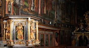 Zdjęcie nr 1: Ambona przyścienna, wisząca, ustawiona na północnym węgarze arkady tęczowej, dostępna przez schody od strony zakrystii. Kosz na planie sześcioboku z wysuniętą w stronę ołtarza częścią prowadzącą do drzwi. Ścianki wydzielone kolumnami o kapitelach korynckich, ustawionymi na postumentach, podtrzymującymi parapet z silnie wysuniętym gzymsem. Między kolumnami płytkie nisze zwieńczone konchami z figurami czterech ewangelistów i Chrystusa. Przyłucza, fryz i cokół dekorowany akantem. Kosz u spodu z podwieszoną szyszką. Wąski zaplecek ujęty pilastrami podtrzymującymi belkowanie. W polu obraz ze św. Janem Nepomucenem w profilowanej ramie w kształcie stojącego prostokąta zamkniętego łukiem nadwieszonym. Przyłucza i fryz dekorowany akantem i rozetami. Baldachim na planie sześcioboku, przedzielony belką arkady tęczowej. Podstawę tworzy belkowanie z wydatnym gzymsem, wyłamane w narożach. Kopuła dekorowana spływami akantowymi oraz girlandami, zwieńczona sześciobocznym cokołem, na którym sześć zwężających się kabłąków utworzonych z ażurowego akantu. Pod baldachimem sześcioboczny kaseton z podwieszoną gołębicą Ducha Świętego. Ambona marmoryzowana w odcieniu ciemnoszarym, ornamentyka i detale architektoniczne złocone, srebrzone i czerwone.