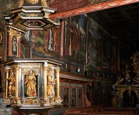 Zdjęcie nr 1: Ambona przyścienna, wisząca, ustawiona na północnym węgarze arkady tęczowej, dostępna przez schody od strony zakrystii. Kosz na planie sześcioboku z wysuniętą w stronę ołtarza częścią prowadzącą do drzwi. Ścianki wydzielone kolumnami o kapitelach korynckich, ustawionymi na postumentach, podtrzymującymi parapet z silnie wysuniętym gzymsem. Między kolumnami płytkie nisze zwieńczone konchami z figurami czterech ewangelistów i Chrystusa. Przyłucza, fryz i cokół dekorowany akantem. Kosz u spodu z podwieszoną szyszką. Wąski zaplecek ujęty pilastrami podtrzymującymi belkowanie. W polu obraz ze św. Janem Nepomucenem w profilowanej ramie w kształcie stojącego prostokąta zamkniętego łukiem nadwieszonym. Przyłucza i fryz dekorowany akantem i rozetami. Baldachim na planie sześcioboku, przedzielony belką arkady tęczowej. Podstawę tworzy belkowanie z wydatnym gzymsem, wyłamane w narożach. Kopuła dekorowana spływami akantowymi oraz girlandami, zwieńczona sześciobocznym cokołem, na którym sześć zwężających się kabłąków utworzonych z ażurowego akantu. Pod baldachimem sześcioboczny kaseton z podwieszoną gołębicą Ducha Świętego. Ambona marmoryzowana w odcieniu ciemnoszarym, ornamentyka i detale architektoniczne złocone, srebrzone i czerwone.