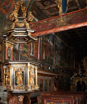 Zdjęcie nr 1: Ambona przyścienna, wisząca, ustawiona na północnym węgarze arkady tęczowej, dostępna przez schody od strony zakrystii. Kosz na planie sześcioboku z wysuniętą w stronę ołtarza częścią prowadzącą do drzwi. Ścianki wydzielone kolumnami o kapitelach korynckich, ustawionymi na postumentach, podtrzymującymi parapet z silnie wysuniętym gzymsem. Między kolumnami płytkie nisze zwieńczone konchami z figurami czterech ewangelistów i Chrystusa. Przyłucza, fryz i cokół dekorowany akantem. Kosz u spodu z podwieszoną szyszką. Wąski zaplecek ujęty pilastrami podtrzymującymi belkowanie. W polu obraz ze św. Janem Nepomucenem w profilowanej ramie w kształcie stojącego prostokąta zamkniętego łukiem nadwieszonym. Przyłucza i fryz dekorowany akantem i rozetami. Baldachim na planie sześcioboku, przedzielony belką arkady tęczowej. Podstawę tworzy belkowanie z wydatnym gzymsem, wyłamane w narożach. Kopuła dekorowana spływami akantowymi oraz girlandami, zwieńczona sześciobocznym cokołem, na którym sześć zwężających się kabłąków utworzonych z ażurowego akantu. Pod baldachimem sześcioboczny kaseton z podwieszoną gołębicą Ducha Świętego. Ambona marmoryzowana w odcieniu ciemnoszarym, ornamentyka i detale architektoniczne złocone, srebrzone i czerwone.