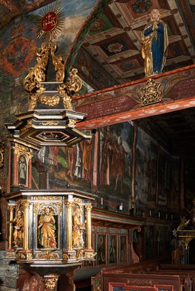 Zdjęcie nr 1: Ambona przyścienna, wisząca, ustawiona na północnym węgarze arkady tęczowej, dostępna przez schody od strony zakrystii. Kosz na planie sześcioboku z wysuniętą w stronę ołtarza częścią prowadzącą do drzwi. Ścianki wydzielone kolumnami o kapitelach korynckich, ustawionymi na postumentach, podtrzymującymi parapet z silnie wysuniętym gzymsem. Między kolumnami płytkie nisze zwieńczone konchami z figurami czterech ewangelistów i Chrystusa. Przyłucza, fryz i cokół dekorowany akantem. Kosz u spodu z podwieszoną szyszką. Wąski zaplecek ujęty pilastrami podtrzymującymi belkowanie. W polu obraz ze św. Janem Nepomucenem w profilowanej ramie w kształcie stojącego prostokąta zamkniętego łukiem nadwieszonym. Przyłucza i fryz dekorowany akantem i rozetami. Baldachim na planie sześcioboku, przedzielony belką arkady tęczowej. Podstawę tworzy belkowanie z wydatnym gzymsem, wyłamane w narożach. Kopuła dekorowana spływami akantowymi oraz girlandami, zwieńczona sześciobocznym cokołem, na którym sześć zwężających się kabłąków utworzonych z ażurowego akantu. Pod baldachimem sześcioboczny kaseton z podwieszoną gołębicą Ducha Świętego. Ambona marmoryzowana w odcieniu ciemnoszarym, ornamentyka i detale architektoniczne złocone, srebrzone i czerwone.