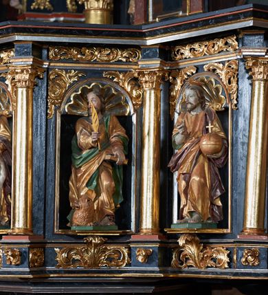 Zdjęcie nr 4: Ambona przyścienna, wisząca, ustawiona na północnym węgarze arkady tęczowej, dostępna przez schody od strony zakrystii. Kosz na planie sześcioboku z wysuniętą w stronę ołtarza częścią prowadzącą do drzwi. Ścianki wydzielone kolumnami o kapitelach korynckich, ustawionymi na postumentach, podtrzymującymi parapet z silnie wysuniętym gzymsem. Między kolumnami płytkie nisze zwieńczone konchami z figurami czterech ewangelistów i Chrystusa. Przyłucza, fryz i cokół dekorowany akantem. Kosz u spodu z podwieszoną szyszką. Wąski zaplecek ujęty pilastrami podtrzymującymi belkowanie. W polu obraz ze św. Janem Nepomucenem w profilowanej ramie w kształcie stojącego prostokąta zamkniętego łukiem nadwieszonym. Przyłucza i fryz dekorowany akantem i rozetami. Baldachim na planie sześcioboku, przedzielony belką arkady tęczowej. Podstawę tworzy belkowanie z wydatnym gzymsem, wyłamane w narożach. Kopuła dekorowana spływami akantowymi oraz girlandami, zwieńczona sześciobocznym cokołem, na którym sześć zwężających się kabłąków utworzonych z ażurowego akantu. Pod baldachimem sześcioboczny kaseton z podwieszoną gołębicą Ducha Świętego. Ambona marmoryzowana w odcieniu ciemnoszarym, ornamentyka i detale architektoniczne złocone, srebrzone i czerwone.