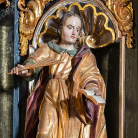 Zdjęcie nr 1: Rzeźba pełnoplastyczna, przedstawiająca św. Jana. Święty zwrócony delikatnie w lewo, ustawiony w kontrapoście z prawą nogą ugiętą w kolanie. Obie ręce ma wyciągnięte na boki, w lewej trzyma otwartą księgę, a w prawej pióro. Twarz młodzieńcza z wysokim czołem, włosy średniej długości z przedziałkiem na środku głowy. Ubrany jest w długą, złotą suknię z zielonym kołnierzem, przepasaną w talii i złoty płaszcz podbity na czerwono, przewieszony przez lewe ramię. Przy lewej nodze orzeł z rozpostartymi skrzydłami. Polichromia naturalistyczna w partiach ciała, szaty złocone.