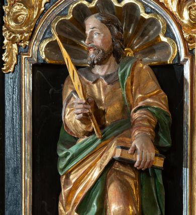Zdjęcie nr 1: Rzeźba pełnoplastyczna, przedstawiająca św. Marka Ewangelistę. Święty ustawiony frontalnie, z głową zwróconą w prawo, z lewą nogą ugiętą w kolanie, księgą w lewej dłoni, którą wspiera o biodro oraz piórem w prawej dłoni.   Twarz pociągła z wysokim czołem, okolona zarostem, włosy średniej długości  z przedziałkiem na środku głowy. Ubrany jest w długą, złotą suknię z brązowym kołnierzem, przepasaną w talii i złoty płaszcz podbity na zielono, przewieszony przez lewe ramię i zawieszony na lewym boku. Przy prawej nodze lew, zwrócony w prawo. Polichromia naturalistyczna w partiach ciała, szaty złocone.