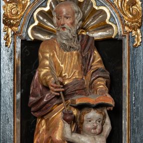 Zdjęcie nr 1: Rzeźba pełnoplastyczna, przedstawiająca św. Mateusza. Figura w delikatnym kontrapoście z prawą nogą ugiętą w kolanie, ustawiona frontalnie, z głową skierowaną w prawą stronę. Lewą ręką podtrzymuje otwartą księgę wspartą na głowie klęczącego u jego lewego boku małego człowieka, zaś prawą trzyma pióro, które macza w kałamarzu znajdującym się w ręku człowieka. Twarz starcza z wysokim czołem, okolona długą i siwą brodą; włosy średniej długości siwe. Ubrany jest w długą, złotą i przepasaną w talii suknię oraz  złoty płaszcz podbity na czerwono, przewieszony przez lewe ramię i zawieszony na prawym boku. Człowiek klęczący na lewym kolanie, z rękami wzniesionymi do góry, w prawej trzyma kałamarz. Twarz pulchna o rysach dziecięcych, włosy krótkie i jasne. Ubrany jest w złoconą tkaninę, przewieszoną przez biodra. Polichromia naturalistyczna w partiach ciała, szaty złocone.