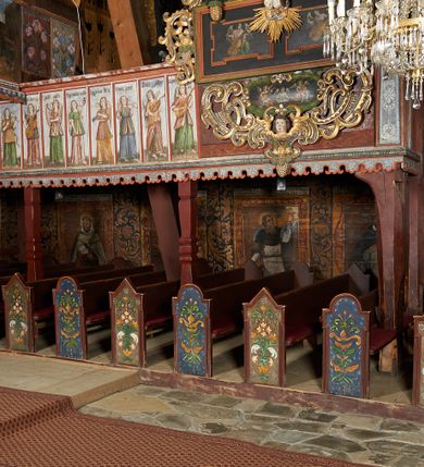 Zdjęcie nr 3: Prospekt organowy podwieszony przy północnej ścianie nawy, oparty na czterech filarach, dostępny z parapetu chóru. Balustrada drewniana z malowaną dekoracją; u spodu pas z ornamentem roślinnym; od frontu podzielona na trzynaście jednofiguralnych przedstawień w ramach, w formie wydłużonych, stojących prostokątów z przedstawieniami aniołów grających na instrumentach. Z boku na balustradzie dwie sceny w formie leżącego prostokąta ze św. Dawidem grającym na lirze i św. Cecylią grająca na organach, oddzielone pasem z dekoracją roślinną. 
Prospekt organowy architektoniczny, pięcioosiowy o bogatej dekoracji snycerskiej. Organy umieszczone na podstawie w kształcie leżącego prostokąta, dekorowanej dwiema płycinami z uszakami w narożach, z malowanymi przedstawieniami grających na instrumentach aniołów oraz z rzeźbionymi uskrzydlonymi główkami anielskimi w glorii pośrodku. Pod cokołem podwieszona dekoracja malarsko-rzeźbiarska nałożona na balustradę chóru. W centrum kompozycji malarskie przedstawienie trzech aniołów (jeden czyta księgę, a dwaj grają na instrumentach) w wieńcu laurowym. Poniżej, rzeźbiona uskrzydlona główka anielska, a całość ujęta ornamentem małżowinowo-chrząstkowym i zakończona u dołu szyszką. Prostokątna podstawa wspiera niski cokół, na którym ustawiona jest trójwieżyczkowa część główna. Środkowa, wyższa wieżyczka jest o przekroju półkolistym, a boczne kątowe o przekroju trójkątnym. Wieżyczki rozdzielają niższe prostokątne płyciny wypełnione piszczałkami. Pod wieżyczkami bocznymi podwieszone są złocone szyszki. Ażurowa dekoracja rzeźbiarska małżowino-chrząstkowa zdobi uszy organu, jest również umieszczona nad płycinami rozdzielającymi wieżyczki. Zwieńczenie tworzą na osiach bocznych strome szczyty, a pośrodku dwugłowy orzeł, na piersi którego w kartuszu w kształcie serca widnieją sygle „A[LBERTUS] B[INKOWICZ] / P[LEBANUS] O[RAVIENSIS]”. Piszczałki przysłaniają od góry ażurowe, rzeźbione firanki o motywie małżowinowo-chrząstkowym, a u dołu wąski pas dekoracji ornamentalnej z motywem silnie przestylizowanych lilii. Organy polichromowane na czarno, profilowania w kolorze czerwonym, zielonym i pomarańczowym, ornamentyka złocona i srebrzona. 



