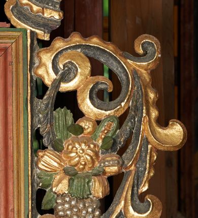 Zdjęcie nr 24: Prospekt organowy podwieszony przy północnej ścianie nawy, oparty na czterech filarach, dostępny z parapetu chóru. Balustrada drewniana z malowaną dekoracją; u spodu pas z ornamentem roślinnym; od frontu podzielona na trzynaście jednofiguralnych przedstawień w ramach, w formie wydłużonych, stojących prostokątów z przedstawieniami aniołów grających na instrumentach. Z boku na balustradzie dwie sceny w formie leżącego prostokąta ze św. Dawidem grającym na lirze i św. Cecylią grająca na organach, oddzielone pasem z dekoracją roślinną. 
Prospekt organowy architektoniczny, pięcioosiowy o bogatej dekoracji snycerskiej. Organy umieszczone na podstawie w kształcie leżącego prostokąta, dekorowanej dwiema płycinami z uszakami w narożach, z malowanymi przedstawieniami grających na instrumentach aniołów oraz z rzeźbionymi uskrzydlonymi główkami anielskimi w glorii pośrodku. Pod cokołem podwieszona dekoracja malarsko-rzeźbiarska nałożona na balustradę chóru. W centrum kompozycji malarskie przedstawienie trzech aniołów (jeden czyta księgę, a dwaj grają na instrumentach) w wieńcu laurowym. Poniżej, rzeźbiona uskrzydlona główka anielska, a całość ujęta ornamentem małżowinowo-chrząstkowym i zakończona u dołu szyszką. Prostokątna podstawa wspiera niski cokół, na którym ustawiona jest trójwieżyczkowa część główna. Środkowa, wyższa wieżyczka jest o przekroju półkolistym, a boczne kątowe o przekroju trójkątnym. Wieżyczki rozdzielają niższe prostokątne płyciny wypełnione piszczałkami. Pod wieżyczkami bocznymi podwieszone są złocone szyszki. Ażurowa dekoracja rzeźbiarska małżowino-chrząstkowa zdobi uszy organu, jest również umieszczona nad płycinami rozdzielającymi wieżyczki. Zwieńczenie tworzą na osiach bocznych strome szczyty, a pośrodku dwugłowy orzeł, na piersi którego w kartuszu w kształcie serca widnieją sygle „A[LBERTUS] B[INKOWICZ] / P[LEBANUS] O[RAVIENSIS]”. Piszczałki przysłaniają od góry ażurowe, rzeźbione firanki o motywie małżowinowo-chrząstkowym, a u dołu wąski pas dekoracji ornamentalnej z motywem silnie przestylizowanych lilii. Organy polichromowane na czarno, profilowania w kolorze czerwonym, zielonym i pomarańczowym, ornamentyka złocona i srebrzona. 



