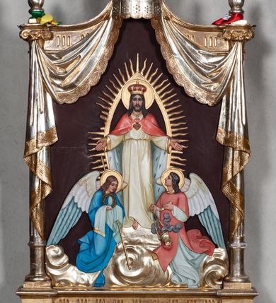 Zdjęcie nr 2: Feretron dwustronny z płaskorzeźbionymi przedstawieniami Matki Boskiej Częstochowskiej i Najświętszego Serca Jezusa, ustawiony na dwóch nóżkach, zaopatrzonych w otwory na drążki do noszenia. Struktura ujęta jest po bokach kolumienkami z kompozytowymi kapitelami, na których ustawione są niewielkie wazony płomieniste. Feretron zwieńczony jest baldachimem i koroną zamkniętą, spiętą sześcioma kabłąkami z zatkniętym u szczytu krzyżykiem na kuli. Tkanina upięta jest pod kapitelami i spływa wzdłuż kolumienek. Po jednej stronie feretronu znajduje się niewielka płaskorzeźba Matki Boskiej Częstochowskiej z podpisem na podłużnej banderoli „POD TWOJĄ OBRONĘ UCIEKAMY SIĘ” umieszczona w owalnej ramie, oplecionej płaskorzeźbioną wicią akantu z muszlą u dołu i palmetą u góry. Po drugiej stronie feretronu umieszczona jest płaskorzeźba Chrystusa stojącego na obłokach z rozłożonymi na boki rękami, adorowanego przez dwa anioły. Chrystusa ukazano na tle promienistej mandorli. Ubrany jest w białą suknię, podwiązaną w talii oraz czerwony płaszcz królewski podbity gronostajem. Na piersiach ma gorejące serce, oplecione koroną cierniową z zatkniętym u góry krzyżykiem, a na głowie koronę zamkniętą. Anioły zwrócone są ku środkowi kompozycji, końcówki skrzydeł mają zielone. Anioł po prawej stronie, ubrany w białą albę i czerwoną dalmatykę trzyma w dłoniach kadzielnicę, natomiast anioł po lewej, ubrany w niebieską suknię trzyma w dłoni koronę cierniową i włócznię. Wszystkie postacie wokół głów mają złote i okrągłe nimby. Płaskorzeźby po obu stronach feretronu umieszczone są na brązowym tle. Struktura oraz ornamenty są złocone i srebrzone. 

