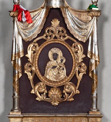 Zdjęcie nr 1: Feretron dwustronny z płaskorzeźbionymi przedstawieniami Matki Boskiej Częstochowskiej i Najświętszego Serca Jezusa, ustawiony na dwóch nóżkach, zaopatrzonych w otwory na drążki do noszenia. Struktura ujęta jest po bokach kolumienkami z kompozytowymi kapitelami, na których ustawione są niewielkie wazony płomieniste. Feretron zwieńczony jest baldachimem i koroną zamkniętą, spiętą sześcioma kabłąkami z zatkniętym u szczytu krzyżykiem na kuli. Tkanina upięta jest pod kapitelami i spływa wzdłuż kolumienek. Po jednej stronie feretronu znajduje się niewielka płaskorzeźba Matki Boskiej Częstochowskiej z podpisem na podłużnej banderoli „POD TWOJĄ OBRONĘ UCIEKAMY SIĘ” umieszczona w owalnej ramie, oplecionej płaskorzeźbioną wicią akantu z muszlą u dołu i palmetą u góry. Po drugiej stronie feretronu umieszczona jest płaskorzeźba Chrystusa stojącego na obłokach z rozłożonymi na boki rękami, adorowanego przez dwa anioły. Chrystusa ukazano na tle promienistej mandorli. Ubrany jest w białą suknię, podwiązaną w talii oraz czerwony płaszcz królewski podbity gronostajem. Na piersiach ma gorejące serce, oplecione koroną cierniową z zatkniętym u góry krzyżykiem, a na głowie koronę zamkniętą. Anioły zwrócone są ku środkowi kompozycji, końcówki skrzydeł mają zielone. Anioł po prawej stronie, ubrany w białą albę i czerwoną dalmatykę trzyma w dłoniach kadzielnicę, natomiast anioł po lewej, ubrany w niebieską suknię trzyma w dłoni koronę cierniową i włócznię. Wszystkie postacie wokół głów mają złote i okrągłe nimby. Płaskorzeźby po obu stronach feretronu umieszczone są na brązowym tle. Struktura oraz ornamenty są złocone i srebrzone. 

