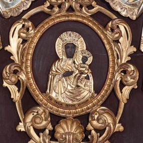 Zdjęcie nr 1: Feretron dwustronny z płaskorzeźbionymi przedstawieniami Matki Boskiej Częstochowskiej i Najświętszego Serca Jezusa, ustawiony na dwóch nóżkach, zaopatrzonych w otwory na drążki do noszenia. Struktura ujęta jest po bokach kolumienkami z kompozytowymi kapitelami, na których ustawione są niewielkie wazony płomieniste. Feretron zwieńczony jest baldachimem i koroną zamkniętą, spiętą sześcioma kabłąkami z zatkniętym u szczytu krzyżykiem na kuli. Tkanina upięta jest pod kapitelami i spływa wzdłuż kolumienek. Po jednej stronie feretronu znajduje się niewielka płaskorzeźba Matki Boskiej Częstochowskiej z podpisem na podłużnej banderoli „POD TWOJĄ OBRONĘ UCIEKAMY SIĘ” umieszczona w owalnej ramie, oplecionej płaskorzeźbioną wicią akantu z muszlą u dołu i palmetą u góry. Po drugiej stronie feretronu umieszczona jest płaskorzeźba Chrystusa stojącego na obłokach z rozłożonymi na boki rękami, adorowanego przez dwa anioły. Chrystusa ukazano na tle promienistej mandorli. Ubrany jest w białą suknię, podwiązaną w talii oraz czerwony płaszcz królewski podbity gronostajem. Na piersiach ma gorejące serce, oplecione koroną cierniową z zatkniętym u góry krzyżykiem, a na głowie koronę zamkniętą. Anioły zwrócone są ku środkowi kompozycji, końcówki skrzydeł mają zielone. Anioł po prawej stronie, ubrany w białą albę i czerwoną dalmatykę trzyma w dłoniach kadzielnicę, natomiast anioł po lewej, ubrany w niebieską suknię trzyma w dłoni koronę cierniową i włócznię. Wszystkie postacie wokół głów mają złote i okrągłe nimby. Płaskorzeźby po obu stronach feretronu umieszczone są na brązowym tle. Struktura oraz ornamenty są złocone i srebrzone. 

