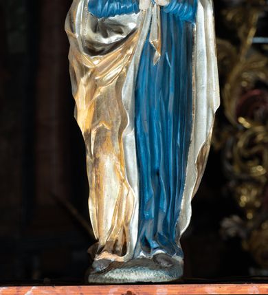 Zdjęcie nr 3: Rzeźba pełna, Chrystus przybity do krzyża trzema gwoździami w lekkim zwisie z głową silnie skręconą w prawo. Twarz podłużna z otwartymi ustami i półprzymkniętymi oczami, okolona kędzierzawą, ciemną brodą; włosy długie spływające na plecy i prawe ramię. Nogi delikatnie ugięte w kolanach; stopy przebite jednym gwoździem, w układzie prawa na lewą. Na głowie Chrystus ma założoną zieloną koronę cierniową. Perizonium w formie tkaniny przewiązanej diagonalnie przez biodra, ze zwisem na prawym boku. Sylwetka wychudzona, smukła, o delikatnym skręcie bioder, z wyraźnie zaznaczonym użyleniem i czerwono-sinymi śladami męki. Polichromia naturalistyczna w partiach ciała, o bladej kolorystyce bieli i błękitu oraz intensywnej czerwonej krwi; perizonium złocone. Nad głową Chrystusa zawieszony zielono-czarny titulus w formie kartusza z napisem „INRI”, ozdobiony motywem małżowinowo-chrząstkowym. Krzyż drewniany, prosty, malowany na czarno. U dołu krzyża zawieszone cztery wota w kształcie złotych serduszek przypiętych czerwonymi kokardkami.