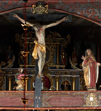 Zdjęcie nr 6: Rzeźba pełna, Matka Boska w pozie stojącej na półkolistym cokole, ukazana frontalnie ze splecionymi na wysokości piersi dłońmi. Twarz pociągła, o delikatnie rzeźbionych rysach, dużych oczach ze wzrokiem skierowanym przed siebie, wyraźnie podkreślonym podbródku. Ubrana jest w niebieską, długą suknię drapowaną w równolegle, rurkowate fałdy i złoty płaszcz przerzucony przez ramiona ze srebrzonym podbiciem. Na głowie ma złoty welon opadający na ramiona. Polichromia w odsłoniętych partiach ciała naturalistyczna.