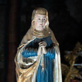 Zdjęcie nr 1: Rzeźba pełna, Matka Boska w pozie stojącej na półkolistym cokole, ukazana frontalnie ze splecionymi na wysokości piersi dłońmi. Twarz pociągła, o delikatnie rzeźbionych rysach, dużych oczach ze wzrokiem skierowanym przed siebie, wyraźnie podkreślonym podbródku. Ubrana jest w niebieską, długą suknię drapowaną w równolegle, rurkowate fałdy i złoty płaszcz przerzucony przez ramiona ze srebrzonym podbiciem. Na głowie ma złoty welon opadający na ramiona. Polichromia w odsłoniętych partiach ciała naturalistyczna.