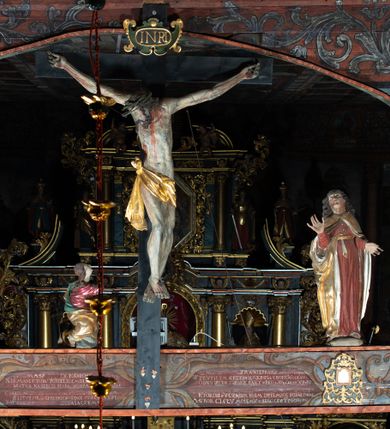 Zdjęcie nr 5: Rzeźba pełna, św. Jan ukazany w pozycji stojącej, frontalnie na półkolistym cokole, z głową zwróconą delikatnie w prawą stronę i uniesioną w górę; ręce ugięte w łokciach, prawa uniesiona. Twarz pełna, oczy zwrócone ku górze, włosy długie, brązowe, w postaci gęstych oddzielnych loków. Święty ubrany jest w długą, ciemnoczerwoną suknię, przepasaną w talii sznurem oraz złoty płaszcz ze srebrzoną podszewką, zapięty u szyi, opadający na ramiona i przewieszony prawym końcem przez pasek w talii. Polichromia w odsłoniętych partiach ciała naturalistyczna.
