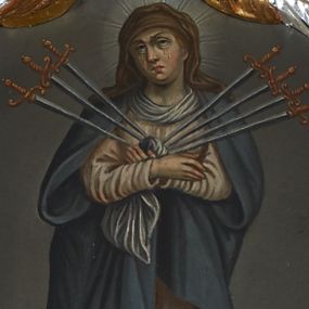 Zdjęcie nr 1: Obraz w formie tonda z całopostaciowym przedstawieniem Matki Boskiej Bolesnej. W centrum kompozycji stojąca Matka Boska, ukazana frontalnie z dłońmi skrzyżowanymi na wysokości piersi, z głową przechyloną w prawo. W jej serce wbite jest siedem mieczy: trzy z lewej strony i cztery z prawej. Twarz trójkątna, oczy otwarte wzniesione ku górze, z których spływają po zaczerwienionych policzkach krople łez. Ubrana jest w różową suknię i szaro-niebieski płaszcz; na głowie ma brązowy welon, a wokół głowy jasny i promienisty nimb. Maria ukazana jest na jednolitym, jasnoszarym tle, u dołu ciemniejszym. Kolorystyka przytłumiona. Rama w kształcie wieńca z wawrzynu, srebrzona, od zewnątrz opleciona złoconą wicią liści akantu.

