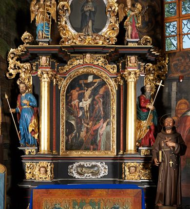 Zdjęcie nr 4: Obraz o formie stojącego prostokąta zamkniętego łukiem półkolistym. Kompozycja wielofiguralna. W centrum postać Chrystusa umarłego, na krzyżu, skierowana trzy czwarte w prawo. Ciało w dużym zwisie, przypominające w układzie literę „Y”, z wyraźnie wydobytą światłocieniem muskulaturą. Perizonium luźno osłaniające biodra, zawiązane na prawym boku; na głowie korona cierniowa. Krzyż prosty, nad głową Chrystusa titulus w formie pionowej banderoli z napisem w języku hebrajskim, greckim i łacińskim „IESVS NAZA/RENVS REX / IVD[A]EORVM”. Po obu stronach Chrystusa ukrzyżowani dwaj łotrzy. Po prawej stronie postać przedstawiona frontalnie, z prawą ręką przełożoną przez ramię krzyża, lewa wyciągnięta wzdłuż ramienia krzyża, z głową skierowaną w stronę Chrystusa. Po lewej stronie  łotr przedstawiony w momencie przybijania do krzyża, z profilu, o łukowato wygiętym ciele, z lewą nogą ugiętą w kolanie. Do jego krzyża podstawiona drabina ujęta diagonalnie. W dolnej partii kompozycji po lewej stronie Longinus w stroju żołnierskim, na siwym koniu ukazanym od tyłu, w skrócie perspektywicznym, przebijający bok Chrystusa włócznią. W lewym, dolnym rogu wyłaniająca się głowa innego czarnego konia, ukazana z profilu. W prawym, dolnym rogu Matka Boska w różowej sukni z szarym płaszczem i ciemną chustą na głowie,  ze splecionymi dłońmi oraz głową odchyloną w lewo. Obok niej po prawej stronie, ukazany w profilu św. Jan w zielonej tunice i czerwonym płaszczu, którego krawędzią wyciera łzy. Sylwetka zwrócona w lewą stronę. Pod krzyżem Chrystusa przyklękająca Maria Magdalena przedstawiona profilem, z rękoma wyciągniętymi ku górze. Ubrana w żółtą suknię z podwiniętymi rękawami. W tle zarys wielu postaci. Niebo czarne. Kolorystyka żywa, intensywna, kontrast plam barwnych; silny światłocień. Rama złocona, drewniana, profilowana, dekorowana ornamentem akantowym na niebieskim tle. 