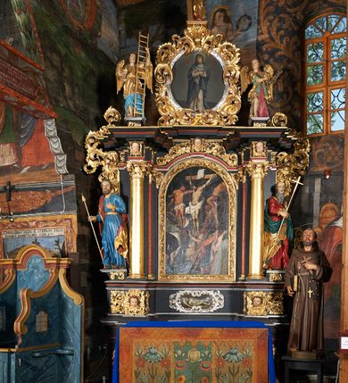 Zdjęcie nr 2: Nastawa architektoniczna, jednoosiowa, jednokondygnacyjna ze zwieńczeniem. Ołtarz prostopadłościenny, drewniany, mensa drewniana z kamiennym portatylem. Antepedium drewniane z malowaną dekoracją w postaci ramy i trzech pól z dekoracją roślinną; zwieńczone od góry lambrekinem. Nastawa ołtarzowa na podwójnym cokole, ujęta zwielokrotnionymi pilastrami, na tle których kolumny o kapitelach kompozytowych, dźwigające belkowanie wyłamane na ich osi o silnie wysuniętym gzymsie. W partii cokołu umieszczony jest obraz przedstawiający Chrystusa w grobie. Pole środkowe nastawy w kształcie stojącego prostokąta zakończonego łukiem półkolistym, w środku obraz „Przebicie włócznią”. Po bokach figury świętych: po lewej św. Jakuba Większego, a po prawej św. Filipa. Zwieńczenie w formie okrągłego pola obrazowego, obwiedzionego srebrną ramą imitującą wieniec laurowy oraz ażurowym, suchym akantem. Na belkowaniu, na osi kolumn ustawione anioły z arma Christi. W polu zwieńczenia obraz Matki Boskiej Bolesnej. Na szczycie figura Chrystusa. Dekorację ornamentalną nastawy stanowią w części dolnej cokołu girlandy, w części cokołowej zasadniczej nastawy liście akantu oraz uskrzydlone główki anielskie na tle akantu; w partii fryzu stylizowane liście akantu, nad kolumnami uskrzydlone główki anielskie. Kondygnacja ujęta uszami utworzonymi z ażurowego akantu. Ołtarz pokryty czarna polichromią z czerwonymi profilami; kolumny oraz partie ornamentalne złocone i srebrzone.