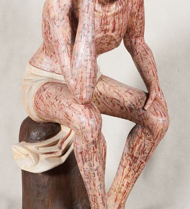 Zdjęcie nr 5: Figura pełnoplastyczna przedstawiająca Chrystusa Frasobliwego. Chrystus ukazany w pozycji siedzącej na drewnianym postumencie, wspierający prawą ręką głowę, a lewą opierający na lewym udzie. Ciało o silnie podkreślonej klatce piersiowej z wąską talią, bardzo szczupłe. Twarz podłużna z długim i wąskim nosem, z głęboko osadzonymi oczami, wzrokiem skierowanym w dół, okolona gęstą, krótką brodą, zawiniętą na końcu w dwa małe pukle. Figura wyrzeźbiona bez włosów. Na głowę założona peruka z długich, naturalnych, jasnych włosów, a na nich korona z przeplecionych gałązek. Perizonium rzeźbione, białe, ciasno oplatające biodra, z jednym końcem rozwianym pod prawym udem. Polichromia w odsłoniętych partiach ciała naturalistyczna. Spod korony cierniowej oraz po całym ciele spływają bardzo liczne, drobne strużki krwi oraz zaznaczone poziomymi kreskami sińce. Na rzeźbę nałożony jest współczesny czerwony płaszcz z materiału, spięty pod szyją metalową klamrą, na brzegach obszyty złotą bordiurą. 


