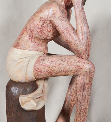 Zdjęcie nr 6: Figura pełnoplastyczna przedstawiająca Chrystusa Frasobliwego. Chrystus ukazany w pozycji siedzącej na drewnianym postumencie, wspierający prawą ręką głowę, a lewą opierający na lewym udzie. Ciało o silnie podkreślonej klatce piersiowej z wąską talią, bardzo szczupłe. Twarz podłużna z długim i wąskim nosem, z głęboko osadzonymi oczami, wzrokiem skierowanym w dół, okolona gęstą, krótką brodą, zawiniętą na końcu w dwa małe pukle. Figura wyrzeźbiona bez włosów. Na głowę założona peruka z długich, naturalnych, jasnych włosów, a na nich korona z przeplecionych gałązek. Perizonium rzeźbione, białe, ciasno oplatające biodra, z jednym końcem rozwianym pod prawym udem. Polichromia w odsłoniętych partiach ciała naturalistyczna. Spod korony cierniowej oraz po całym ciele spływają bardzo liczne, drobne strużki krwi oraz zaznaczone poziomymi kreskami sińce. Na rzeźbę nałożony jest współczesny czerwony płaszcz z materiału, spięty pod szyją metalową klamrą, na brzegach obszyty złotą bordiurą. 


