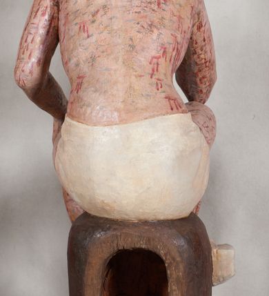 Zdjęcie nr 7: Figura pełnoplastyczna przedstawiająca Chrystusa Frasobliwego. Chrystus ukazany w pozycji siedzącej na drewnianym postumencie, wspierający prawą ręką głowę, a lewą opierający na lewym udzie. Ciało o silnie podkreślonej klatce piersiowej z wąską talią, bardzo szczupłe. Twarz podłużna z długim i wąskim nosem, z głęboko osadzonymi oczami, wzrokiem skierowanym w dół, okolona gęstą, krótką brodą, zawiniętą na końcu w dwa małe pukle. Figura wyrzeźbiona bez włosów. Na głowę założona peruka z długich, naturalnych, jasnych włosów, a na nich korona z przeplecionych gałązek. Perizonium rzeźbione, białe, ciasno oplatające biodra, z jednym końcem rozwianym pod prawym udem. Polichromia w odsłoniętych partiach ciała naturalistyczna. Spod korony cierniowej oraz po całym ciele spływają bardzo liczne, drobne strużki krwi oraz zaznaczone poziomymi kreskami sińce. Na rzeźbę nałożony jest współczesny czerwony płaszcz z materiału, spięty pod szyją metalową klamrą, na brzegach obszyty złotą bordiurą. 


