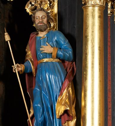Zdjęcie nr 1: Rzeźba pełna, przedstawiająca św. Jakuba Większego. Święty delikatnie zwrócony w prawo, z prawą nogą ugiętą w kolanie, lewą ręką ma złożoną na piersi, w prawej trzyma kij pielgrzyma. Twarz podłużna z dużymi oczami i długim nosem, okolona bujną, brązową i krótką brodą oraz krótkimi włosami. Święty ubrany jest w niebieską suknię, obficie drapowaną u dołu, przewiązaną w talii złotym paskiem oraz złocony płaszcz z czerwoną podszewką, odsłaniający lewe ramię; na stopach ma założone brązowe buty. Polichromia w odsłoniętych partiach ciała naturalistyczna, płaszcz i laska złocone.