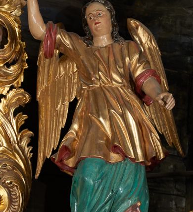 Zdjęcie nr 3: Obraz w kształcie owalu przedstawiający Świętą Rodzinę ukazaną na tle wnętrza. Po lewej stronie siedzący na krześle ustawionym na podeście św. Józef z Dzieciątkiem. Twarz świętego o rysach dojrzałego mężczyzny z długim nosem, okolona siwą brodą i włosami. Ubrany jest czerwone spodnie, szarą suknię, ugrowy płaszcz i sandały. Dzieciątko ukazane jest w pozycji siedzącej, zwrócone trzy czwarte w prawo z głową odchyloną w lewo i szeroko rozłożonymi rękami. Twarz o rysach dziecięcych, pulchnych i zarumienionych policzkach z podkreślonym podbródkiem; włosy kędzierzawe. Ubrane jest w białą sukienkę, przewiązaną czerwonym paskiem. Po prawej stronie obrazu Matka Boska wstępująca jedną nogą na podest, podtrzymująca obiema rękami Dzieciątko. Maria ukazana jest w pozycji stojącej, zwrócona trzy czwarte w prawo. Twarz pełna o jasnej karnacji, oczy przymknięte, nos długi i prosty, włosy upięte z tyłu głowy. Ubrana jest w długą, różową suknię, ciemnobłękitny płaszcz okrywający plecy i ramiona oraz sandały. Nad głowami wszystkich postaci koliste nimby. Powyżej grupy, pośród obłoków ukazane dwa nagie, uskrzydlone putta trzymające koronę, wieniec oraz lilię na tle obłoków. Postacie flankują dwa stojące we wnętrzu wazony z liliami. Kolorystyka przytłumiona, brunatna; szaty wydobyte światłocieniem.