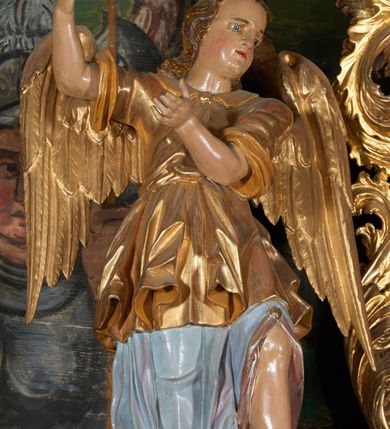 Zdjęcie nr 2: Obraz w kształcie owalu przedstawiający Świętą Rodzinę ukazaną na tle wnętrza. Po lewej stronie siedzący na krześle ustawionym na podeście św. Józef z Dzieciątkiem. Twarz świętego o rysach dojrzałego mężczyzny z długim nosem, okolona siwą brodą i włosami. Ubrany jest czerwone spodnie, szarą suknię, ugrowy płaszcz i sandały. Dzieciątko ukazane jest w pozycji siedzącej, zwrócone trzy czwarte w prawo z głową odchyloną w lewo i szeroko rozłożonymi rękami. Twarz o rysach dziecięcych, pulchnych i zarumienionych policzkach z podkreślonym podbródkiem; włosy kędzierzawe. Ubrane jest w białą sukienkę, przewiązaną czerwonym paskiem. Po prawej stronie obrazu Matka Boska wstępująca jedną nogą na podest, podtrzymująca obiema rękami Dzieciątko. Maria ukazana jest w pozycji stojącej, zwrócona trzy czwarte w prawo. Twarz pełna o jasnej karnacji, oczy przymknięte, nos długi i prosty, włosy upięte z tyłu głowy. Ubrana jest w długą, różową suknię, ciemnobłękitny płaszcz okrywający plecy i ramiona oraz sandały. Nad głowami wszystkich postaci koliste nimby. Powyżej grupy, pośród obłoków ukazane dwa nagie, uskrzydlone putta trzymające koronę, wieniec oraz lilię na tle obłoków. Postacie flankują dwa stojące we wnętrzu wazony z liliami. Kolorystyka przytłumiona, brunatna; szaty wydobyte światłocieniem.