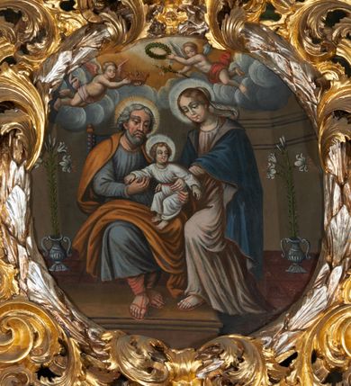Zdjęcie nr 5: Obraz w kształcie owalu przedstawiający Świętą Rodzinę ukazaną na tle wnętrza. Po lewej stronie siedzący na krześle ustawionym na podeście św. Józef z Dzieciątkiem. Twarz świętego o rysach dojrzałego mężczyzny z długim nosem, okolona siwą brodą i włosami. Ubrany jest czerwone spodnie, szarą suknię, ugrowy płaszcz i sandały. Dzieciątko ukazane jest w pozycji siedzącej, zwrócone trzy czwarte w prawo z głową odchyloną w lewo i szeroko rozłożonymi rękami. Twarz o rysach dziecięcych, pulchnych i zarumienionych policzkach z podkreślonym podbródkiem; włosy kędzierzawe. Ubrane jest w białą sukienkę, przewiązaną czerwonym paskiem. Po prawej stronie obrazu Matka Boska wstępująca jedną nogą na podest, podtrzymująca obiema rękami Dzieciątko. Maria ukazana jest w pozycji stojącej, zwrócona trzy czwarte w prawo. Twarz pełna o jasnej karnacji, oczy przymknięte, nos długi i prosty, włosy upięte z tyłu głowy. Ubrana jest w długą, różową suknię, ciemnobłękitny płaszcz okrywający plecy i ramiona oraz sandały. Nad głowami wszystkich postaci koliste nimby. Powyżej grupy, pośród obłoków ukazane dwa nagie, uskrzydlone putta trzymające koronę, wieniec oraz lilię na tle obłoków. Postacie flankują dwa stojące we wnętrzu wazony z liliami. Kolorystyka przytłumiona, brunatna; szaty wydobyte światłocieniem.